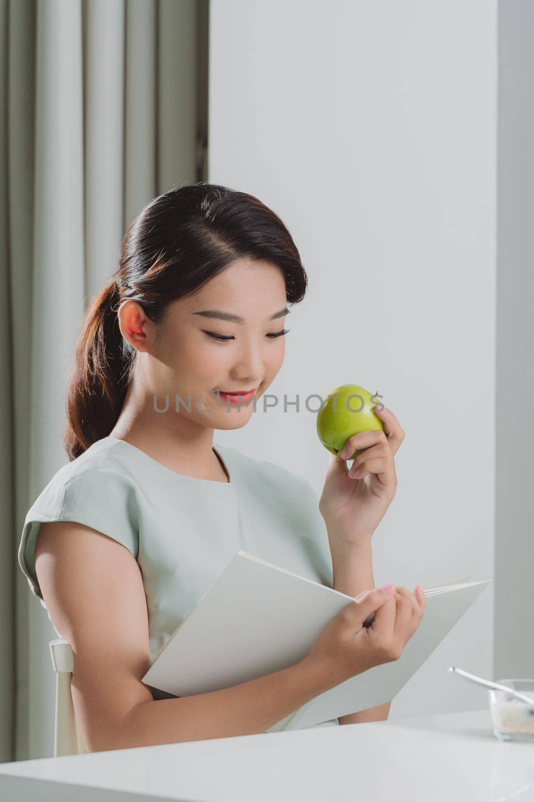 Asian woman reading a book and hold green apple in the home