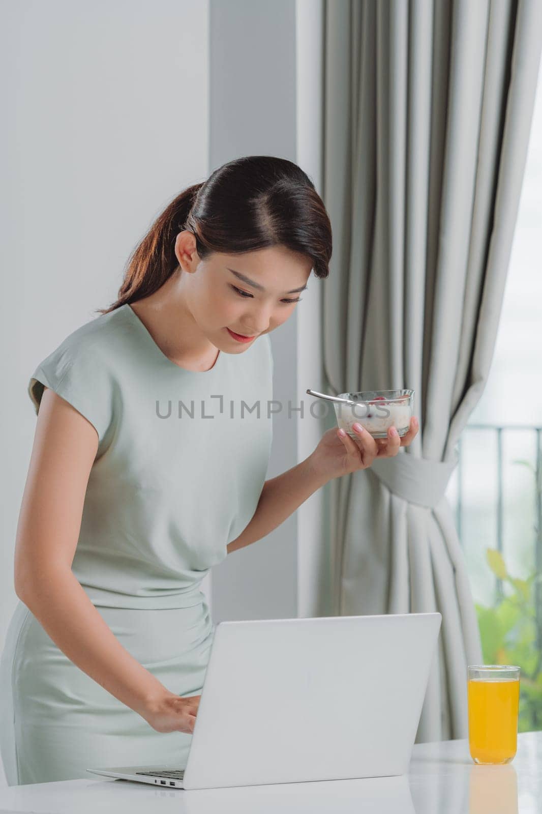 Satisfied woman eating breakfast using a laptop on a desk at home
