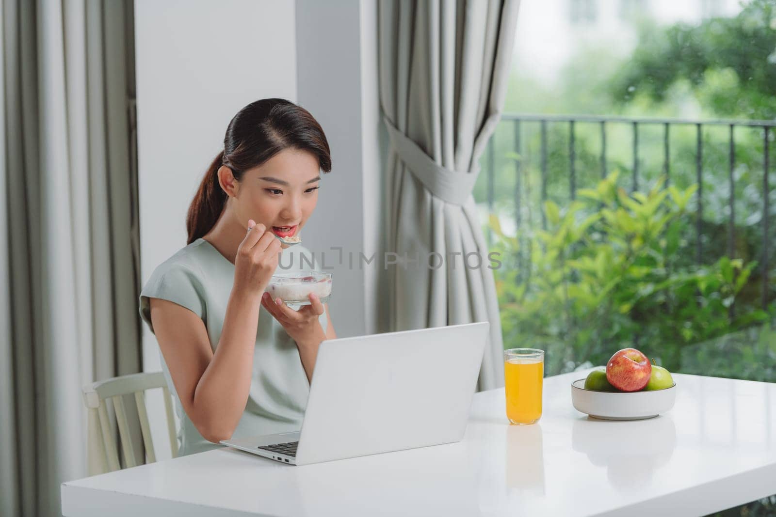 Smiling woman eating breakfast and looking at laptop on table