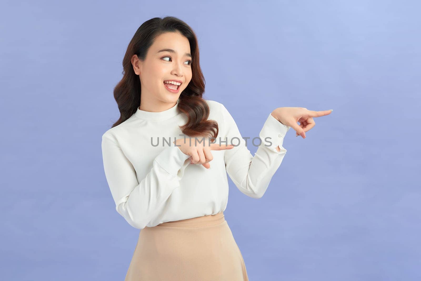 Asian young woman makes gesture two fingers pointed sideways above presenting product something