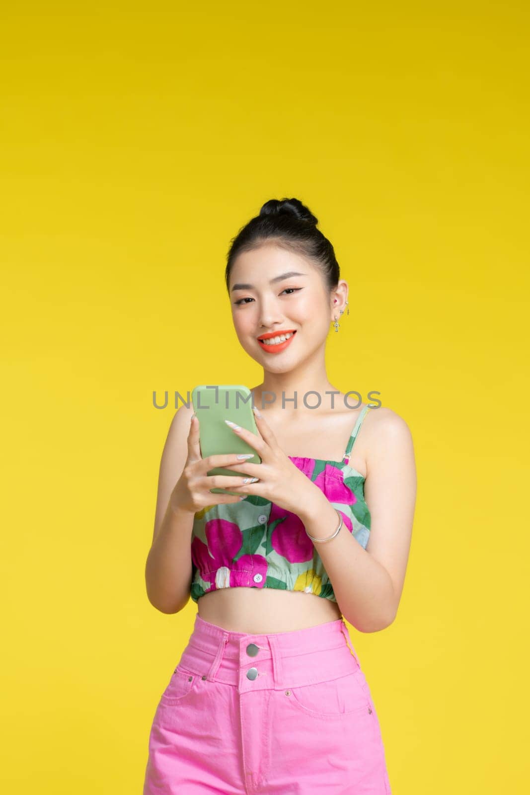 Portrait of a smiling casual woman holding mobile phone over yellow background
