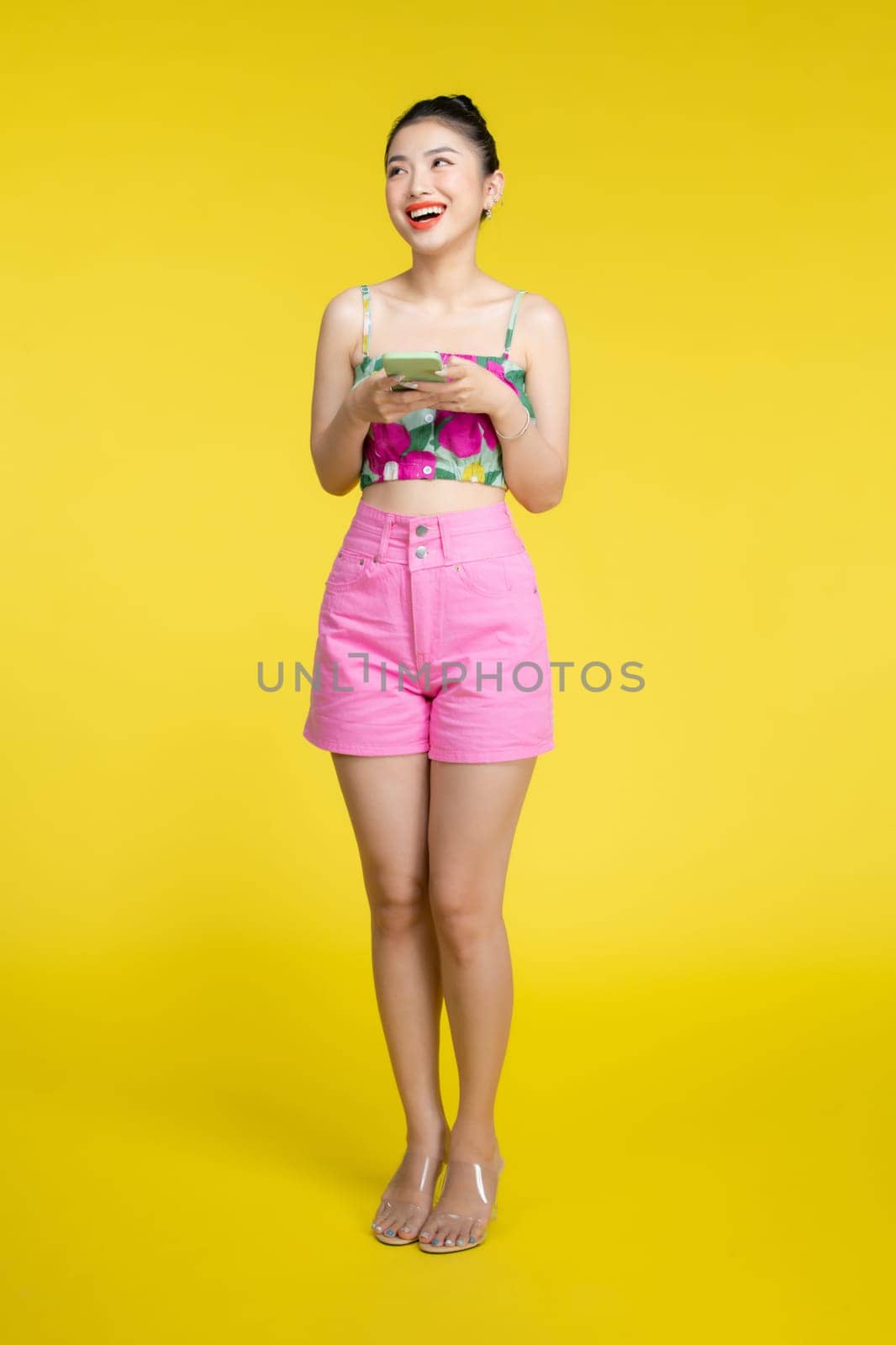 Beautiful Asian woman holding smartphone and smiling on light yellow background by makidotvn