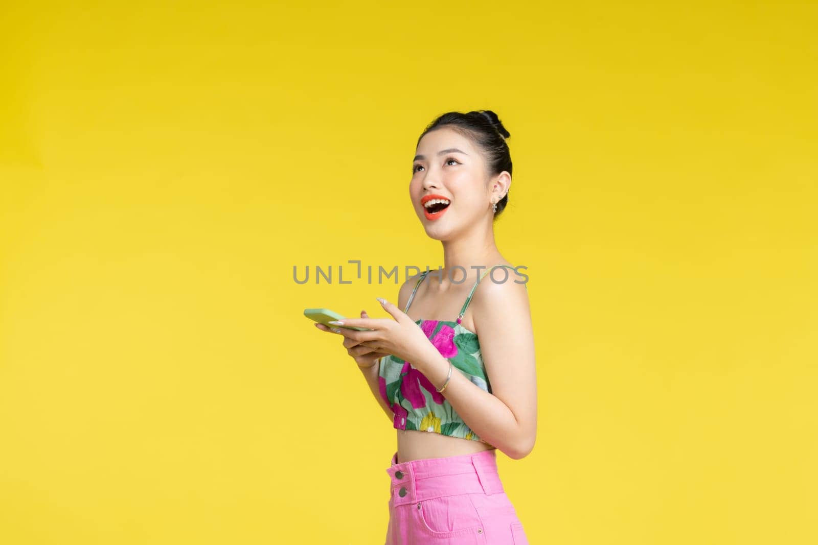 Beautiful Asian woman holding smartphone and smiling with mobile, light yellow background