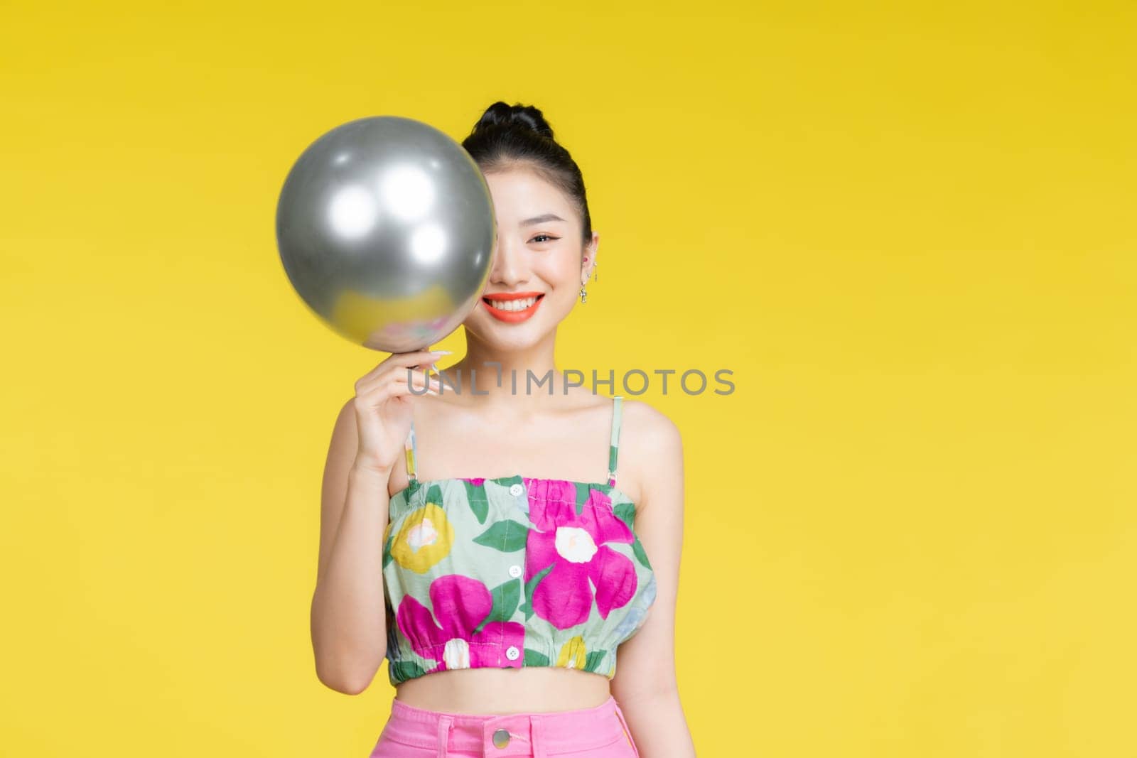 Young asian woman in trendy dress holding silver balloon in her hands