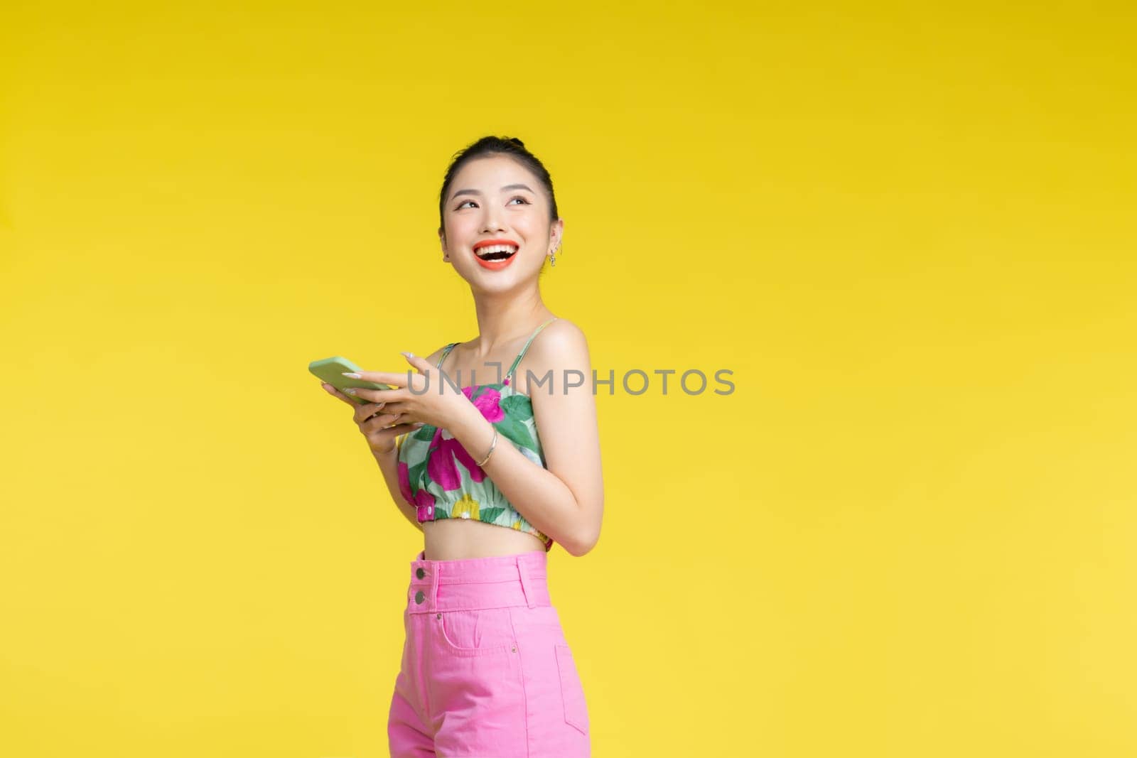 cheerful girl smiling while chatting on smartphone isolated on yellow