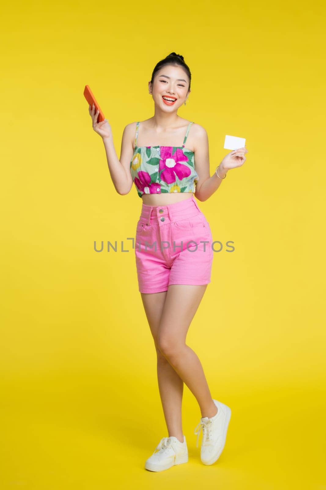 Cheerful beautiful female with credit card and smartphone smiling at camera