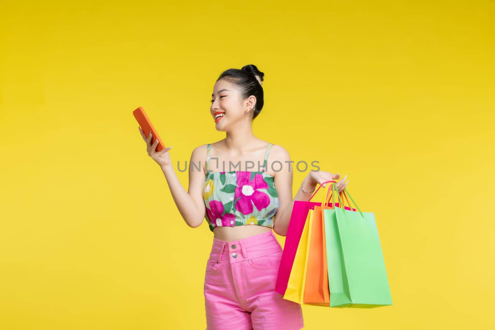 Young energetic Asian woman holding blank use smartphone searching shop retail with colorful shopping bags 