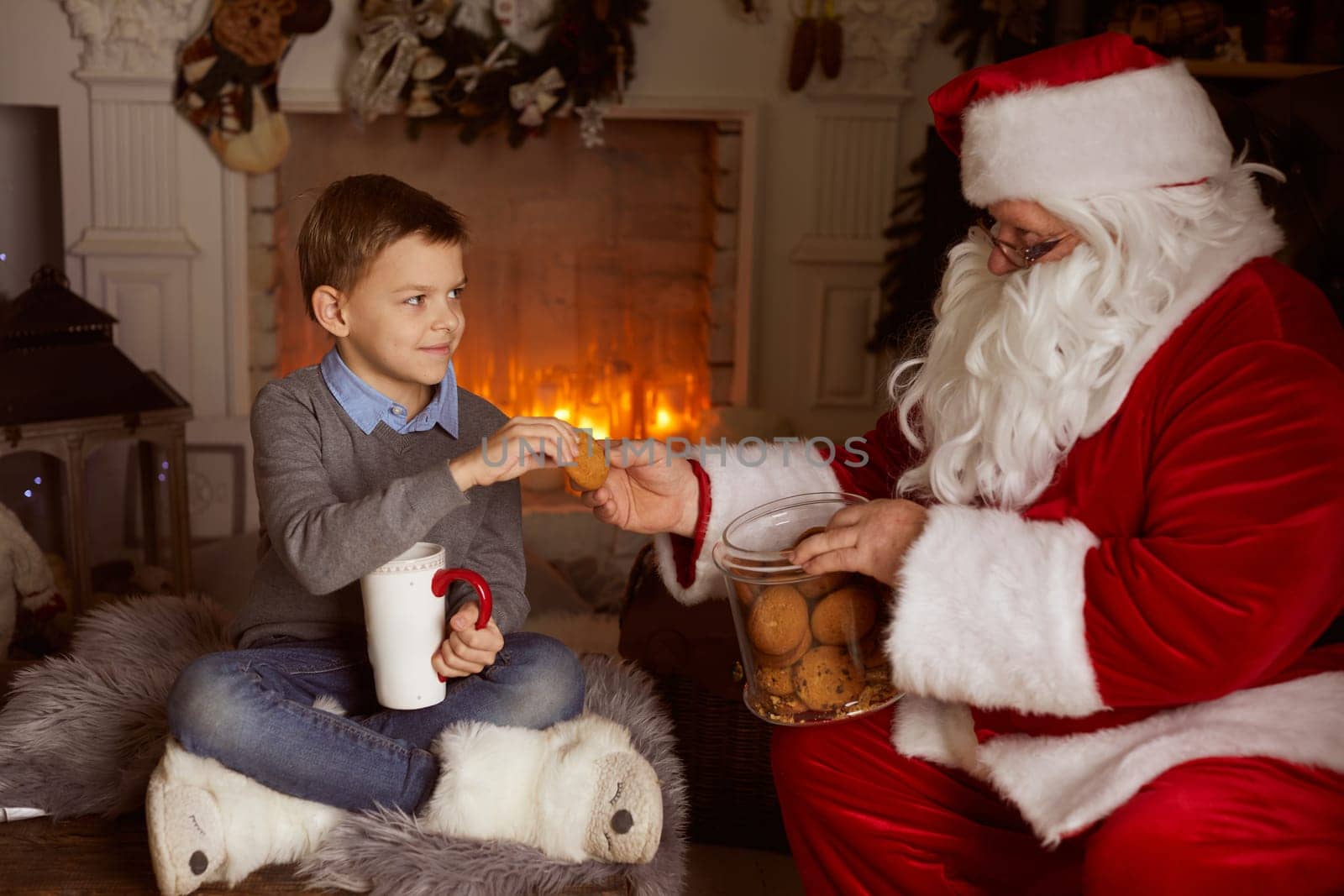 Santa Claus treats a boy with oatmeal cookies against the background of a fireplace and a Christmas tree, New Year's holiday, Christmas