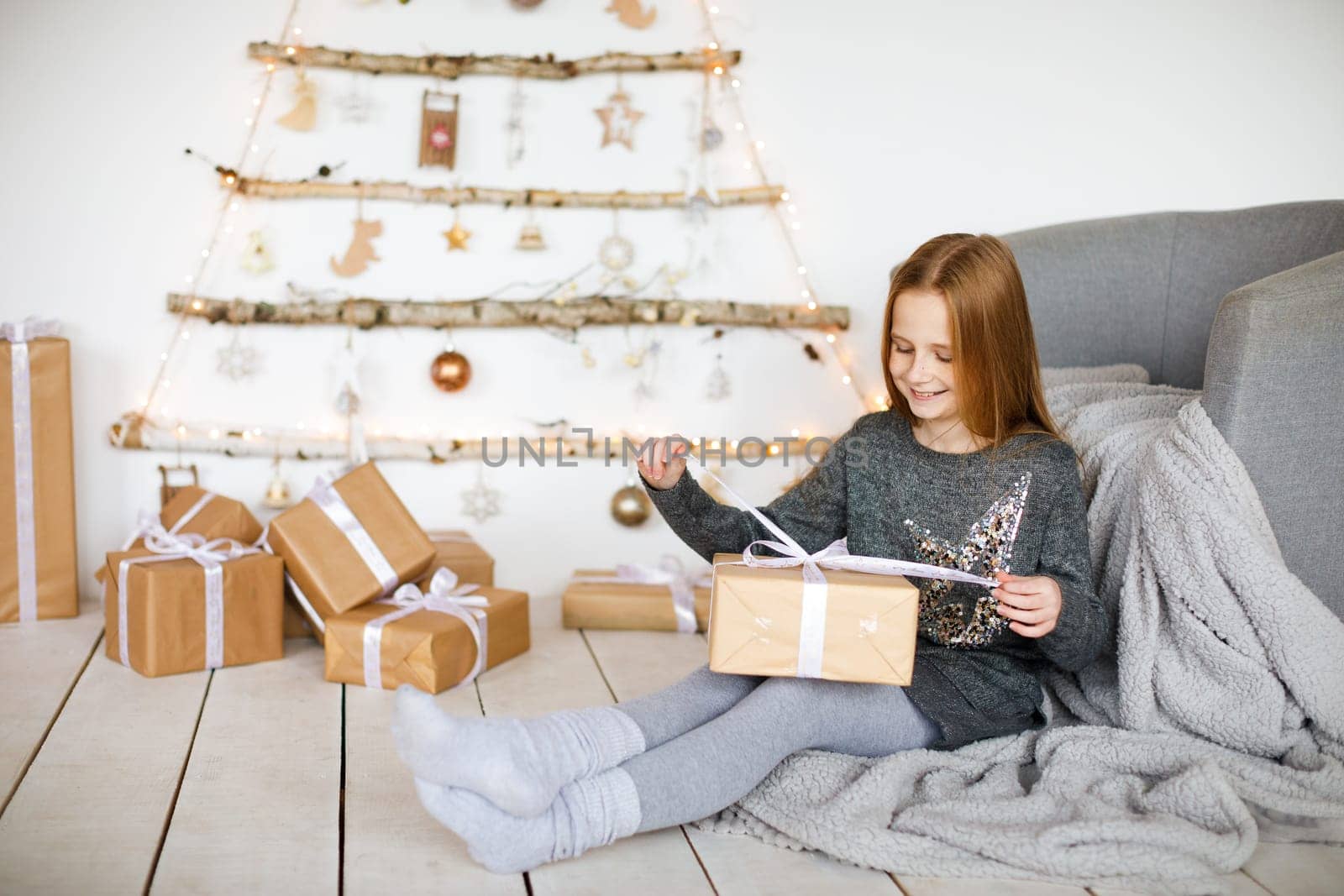 little girl holding craft gift against background of christmas tree with wooden new year toys hanging on wall