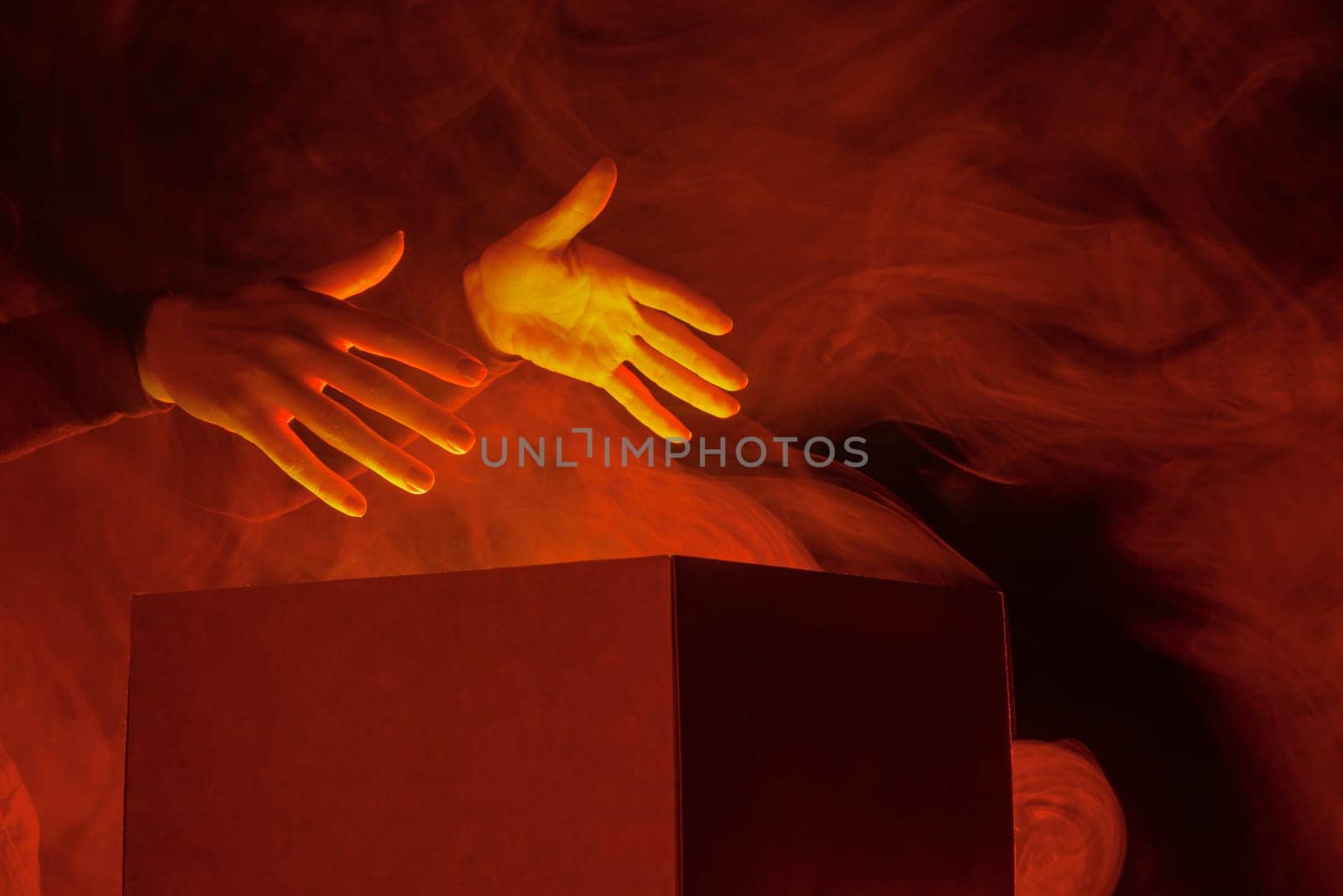 human hands taking out surprise from mysterious box on dark red background surrounded by smoke, mystery box