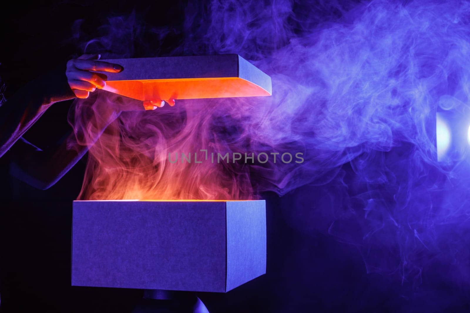 human hands taking out surprise from mysterious box on dark red background surrounded by smoke, mystery box