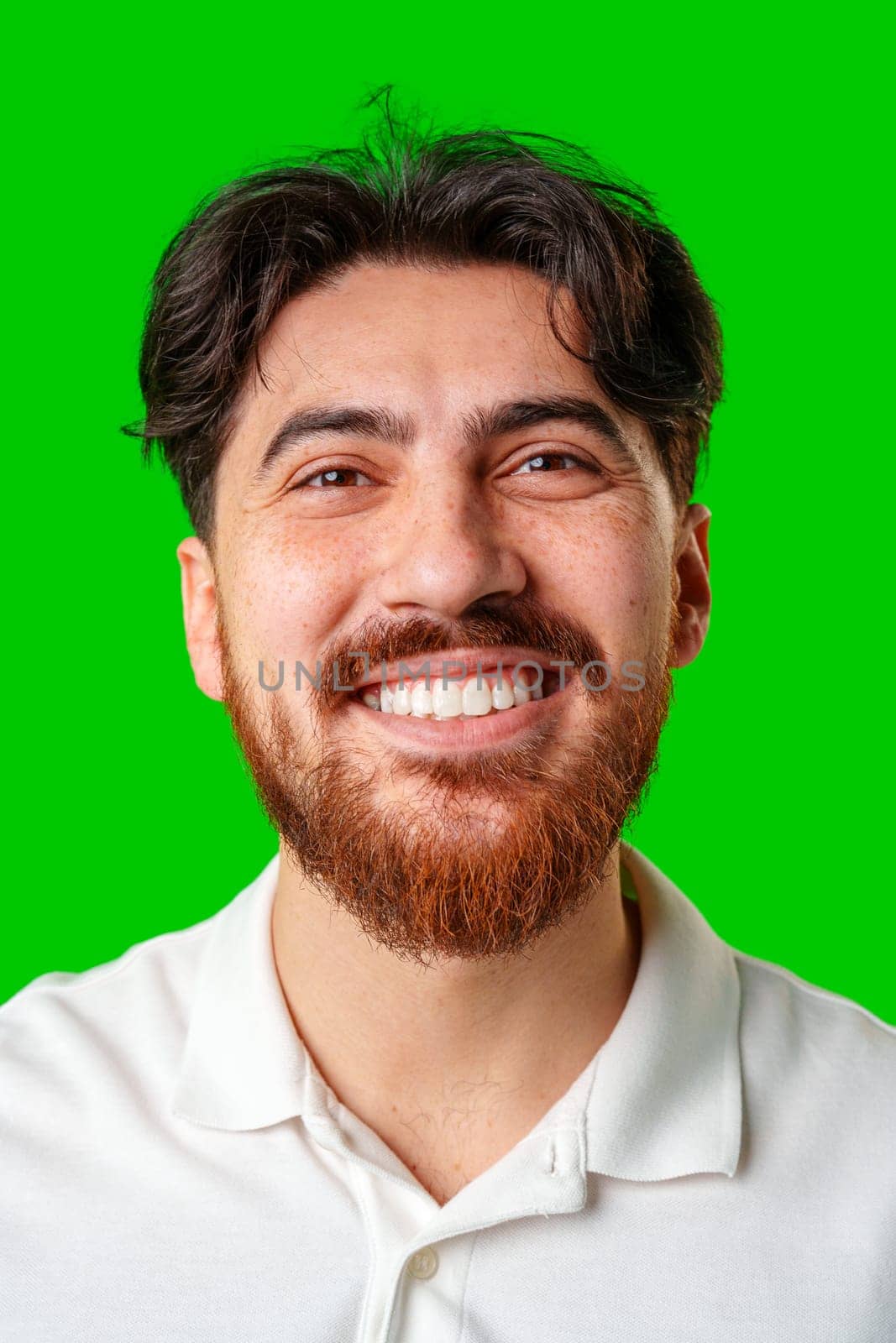 A smiling young man with a beard poses against a bright green background close up