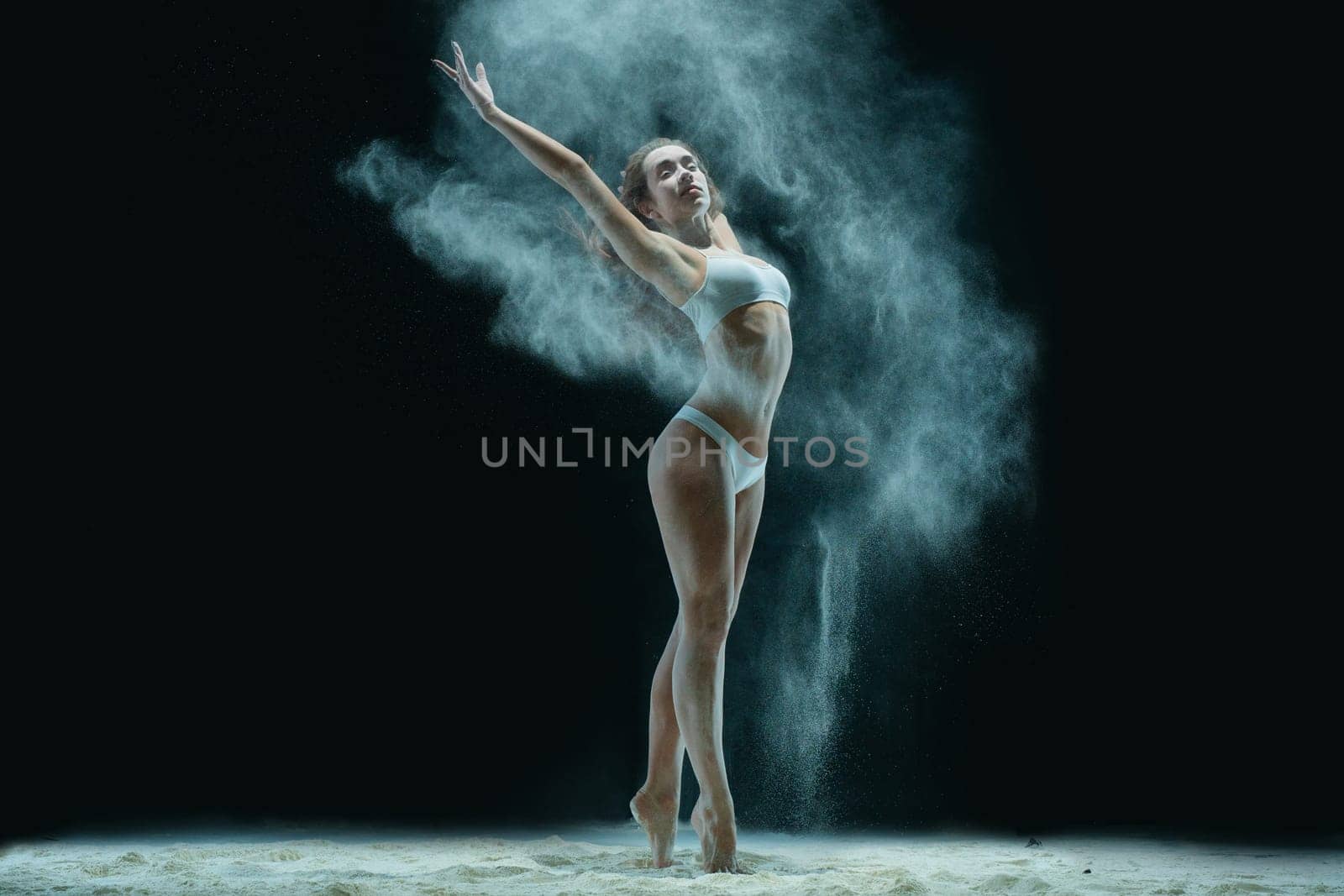 Slim girl wearing lingerie jumping gracefully in white dust cloud view in the dark room