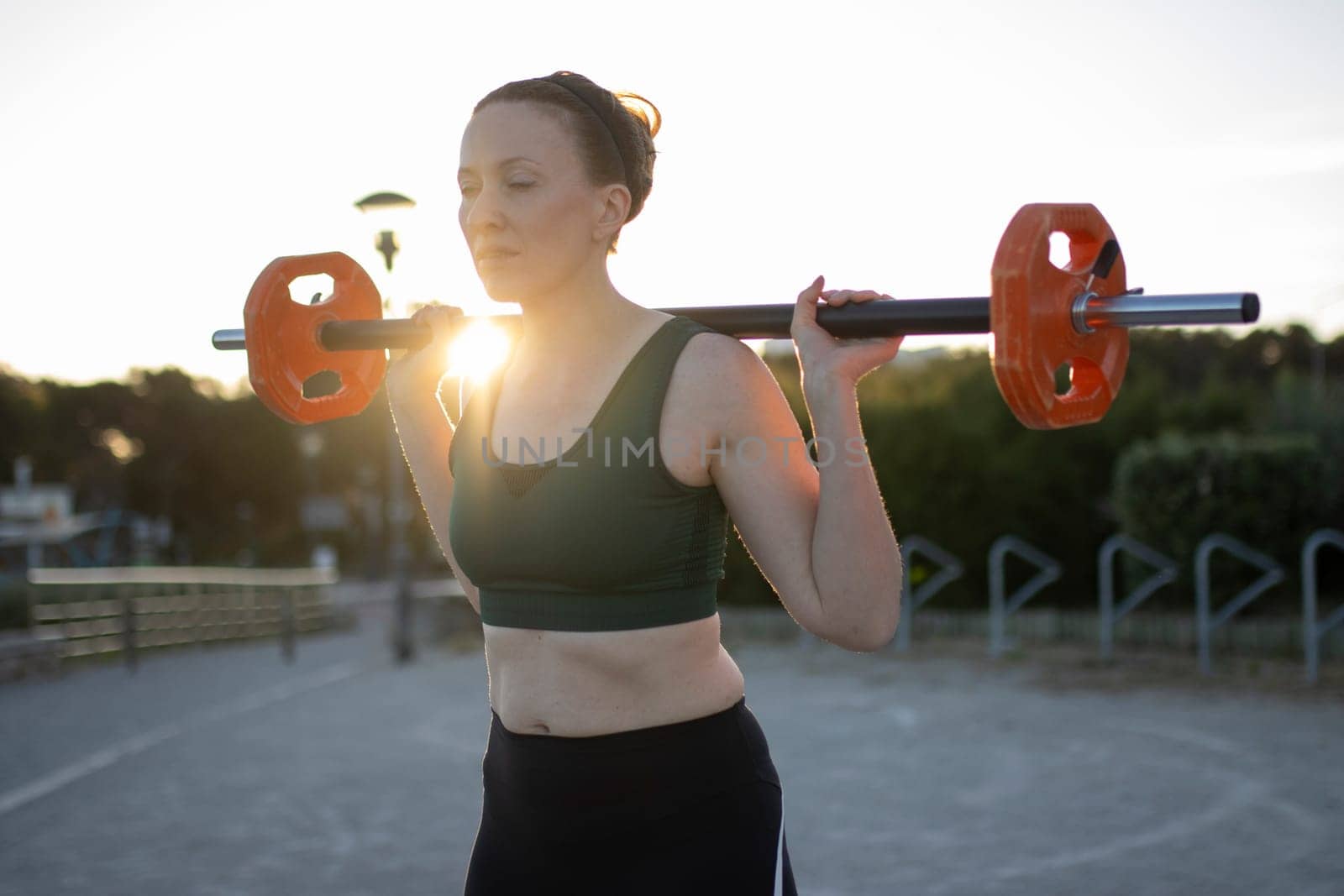 Sportswoman is lifting weights during an outdoor training at sunset