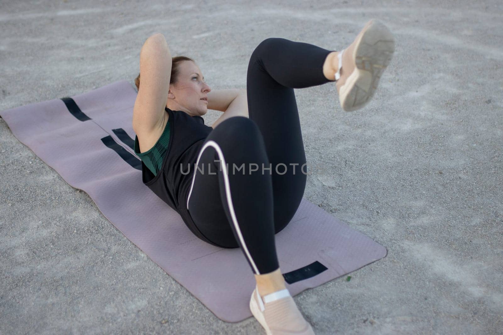Woman is training her abdominal muscles, lying on a fitness mat in an outdoor workout
