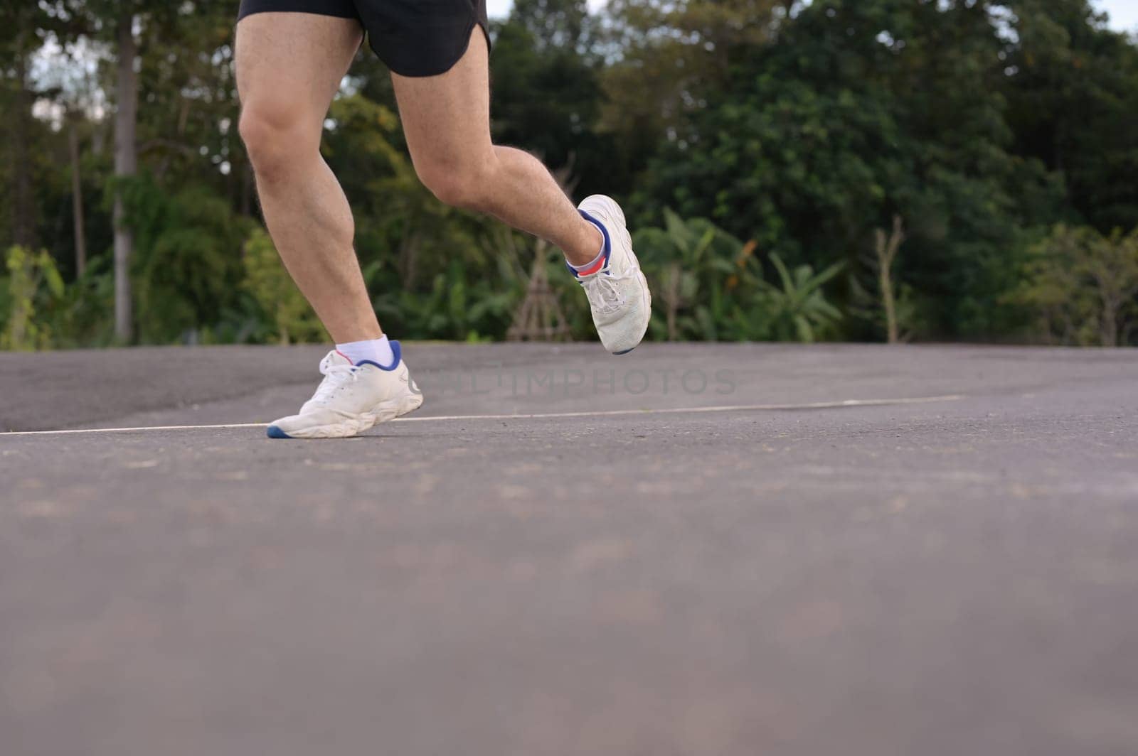 Low angle shot sportsman legs in sport shoes jogging along a paved road. Fitness and active lifestyle.