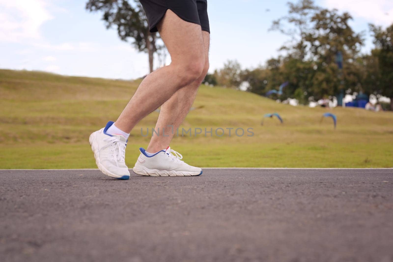 Close up of runner legs and feet moving along a paved path in an outdoor. Fitness and active lifestyle.