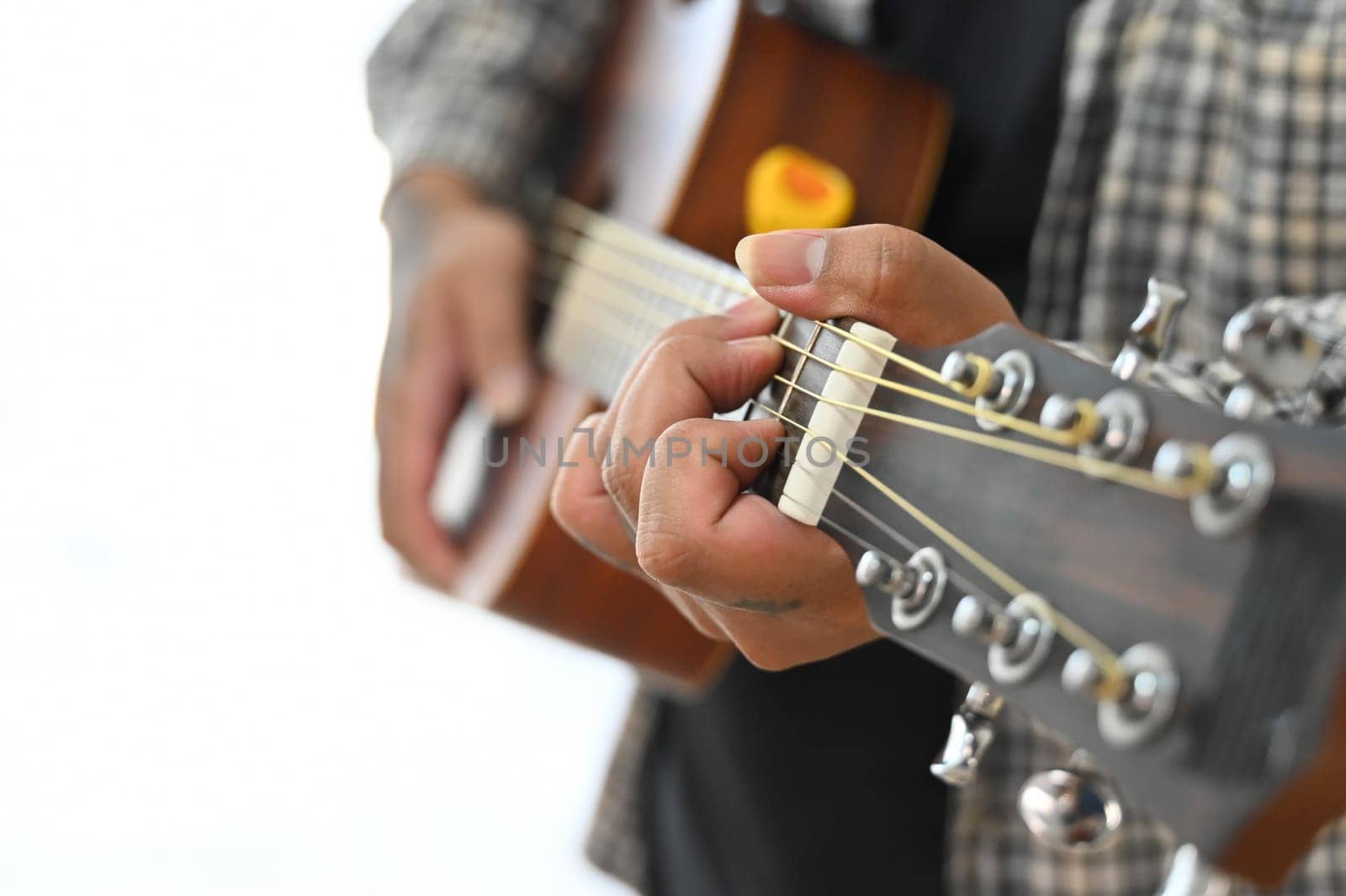 Man in plaid shirt playing an acoustic guitar on sofa at home. Leisure, hobby and activity concept.