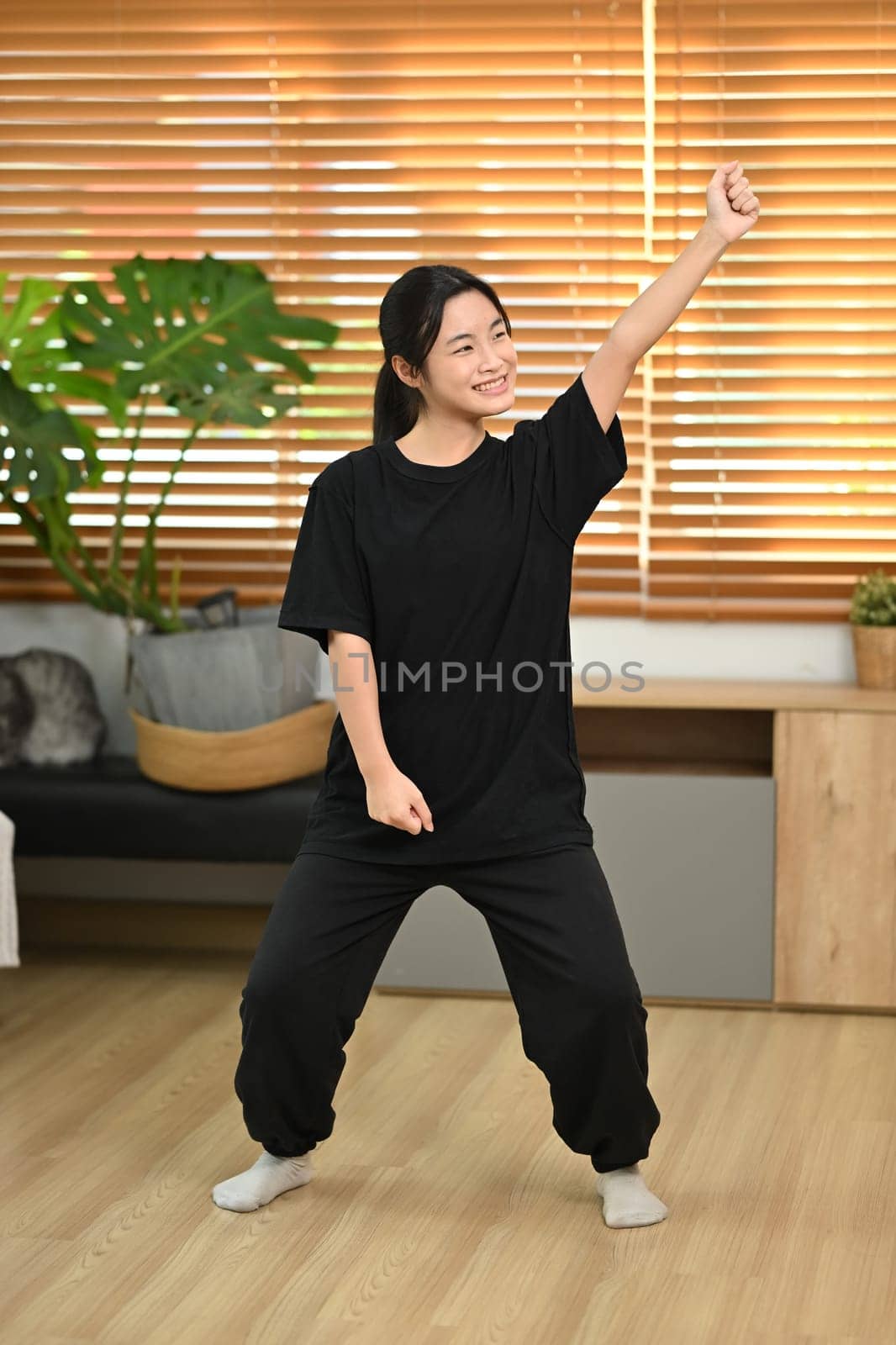 Cheerful young asian woman having fun, practicing a dance move in a living room.