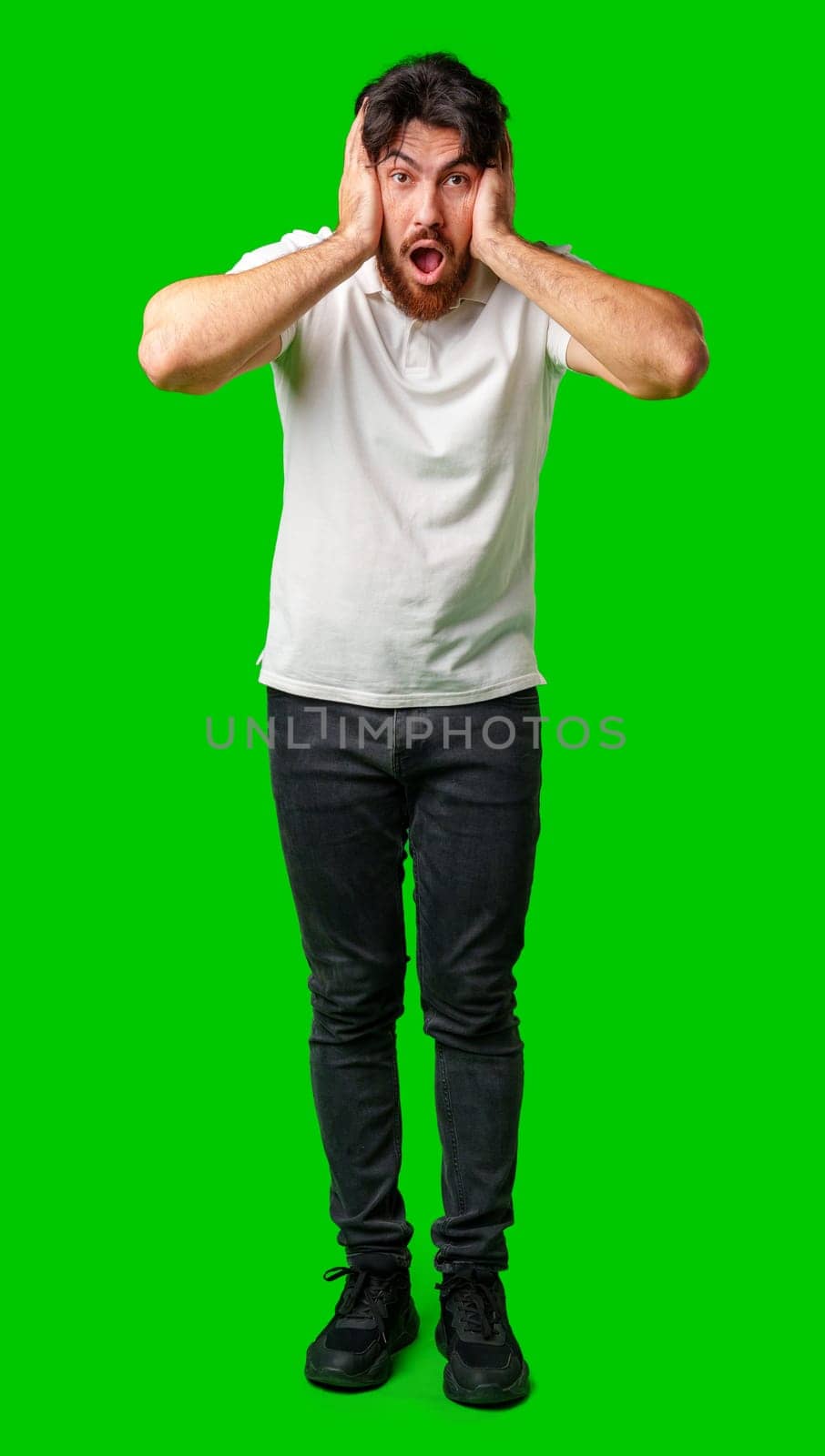 A man with a surprised expression holds his face while against a vibrant green background close up