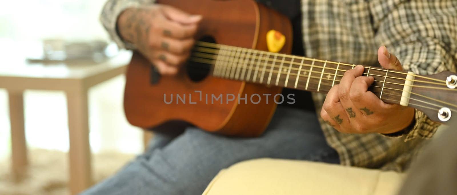Young man playing an acoustic guitar while sitting on sofa at home. Leisure activity and hobby concept.