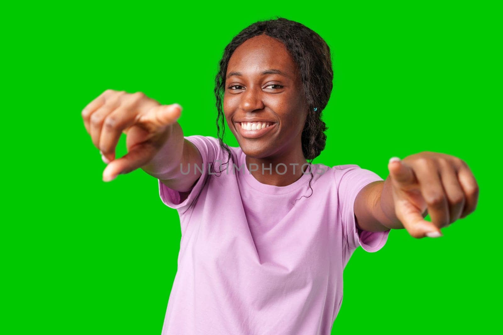 A young woman playfully pointing with a smile against a bright green background in studio