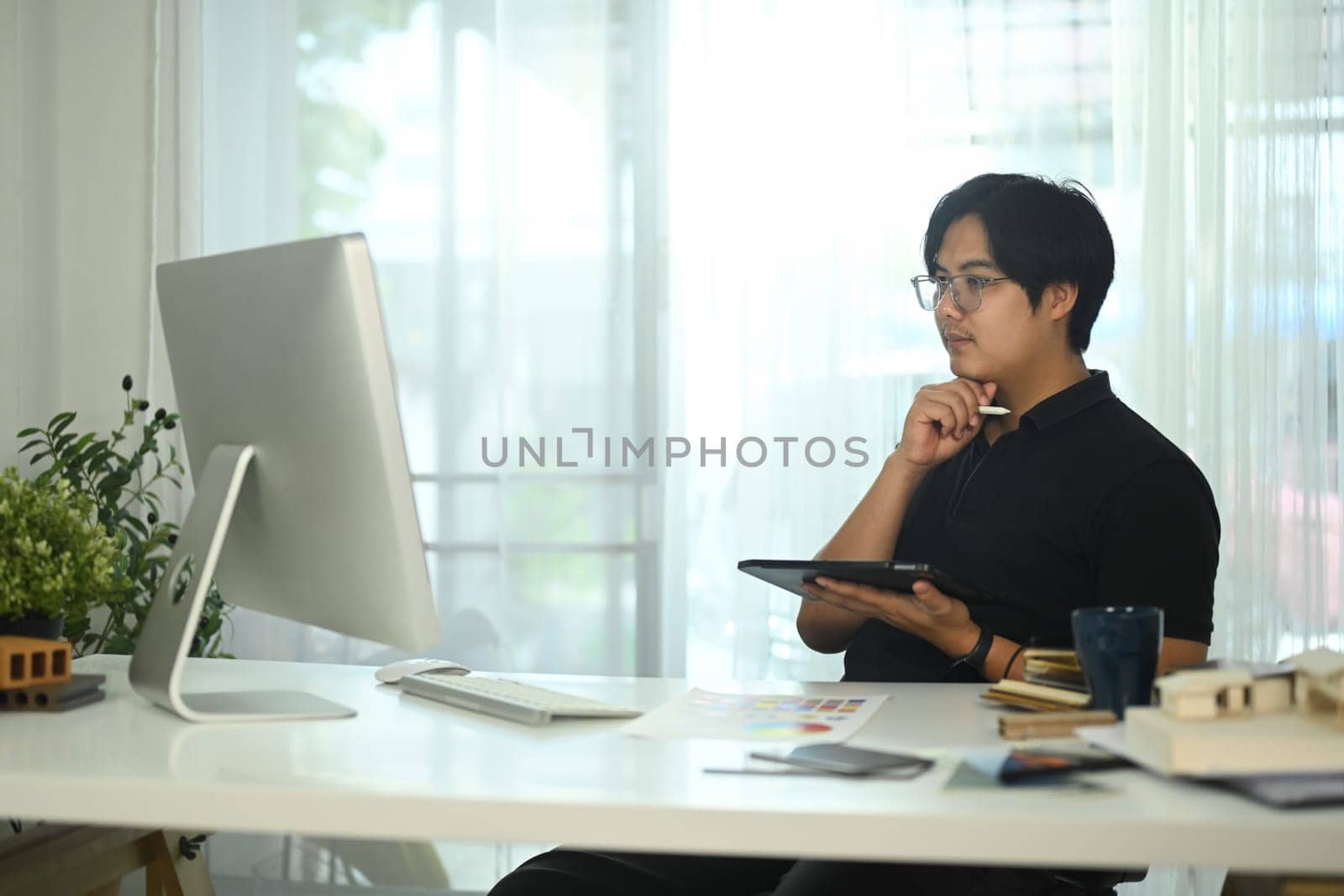 Concentrated architect holding digital tablet planning home design project online in the office.