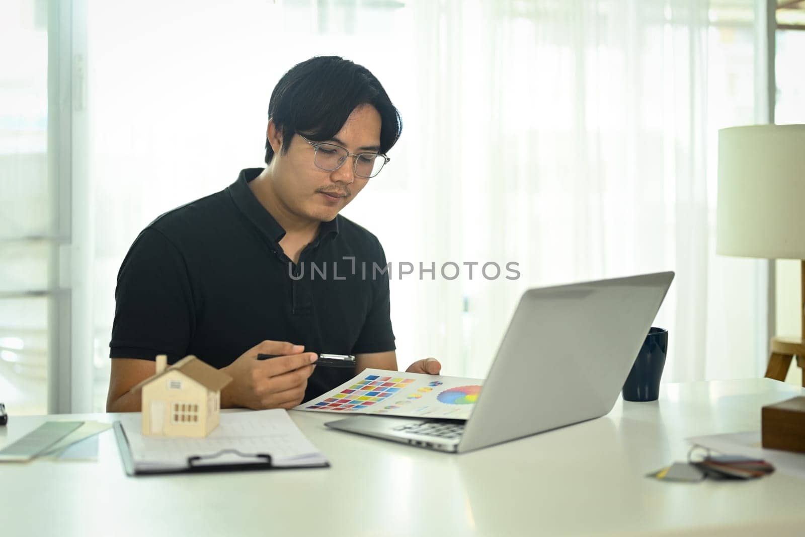 Professional interior designer working with color swatches and planning home design project online on his laptop.