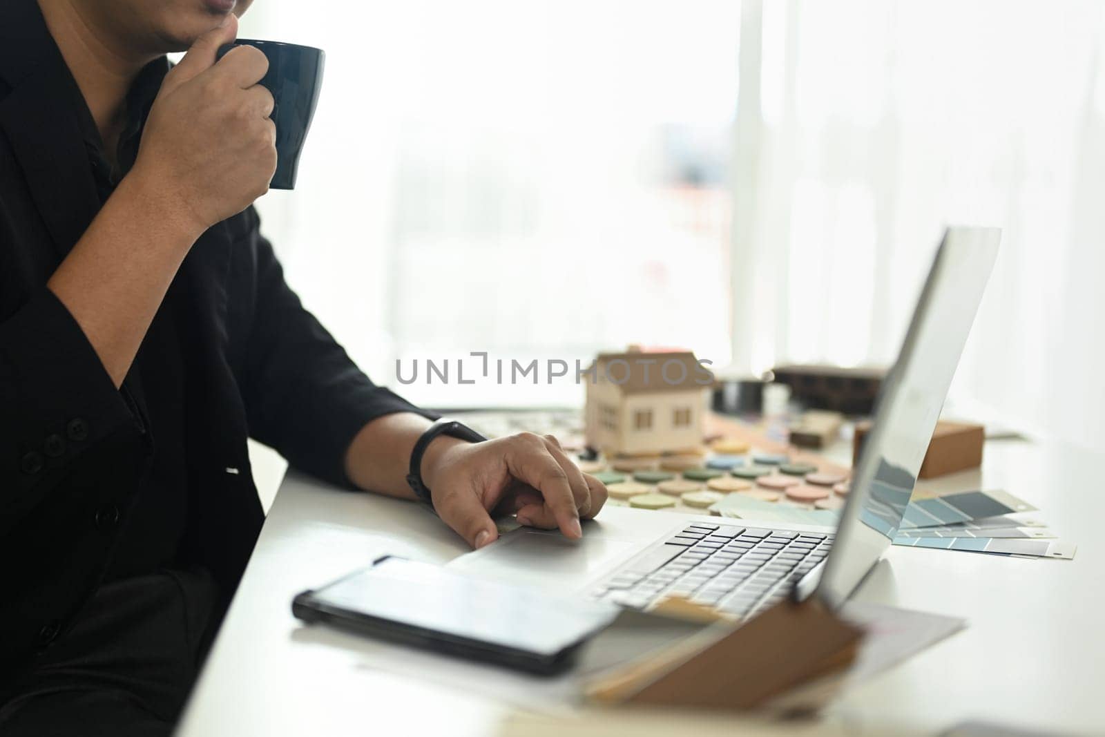Professional interior designer working with color swatches and planning home design project online on his laptop.