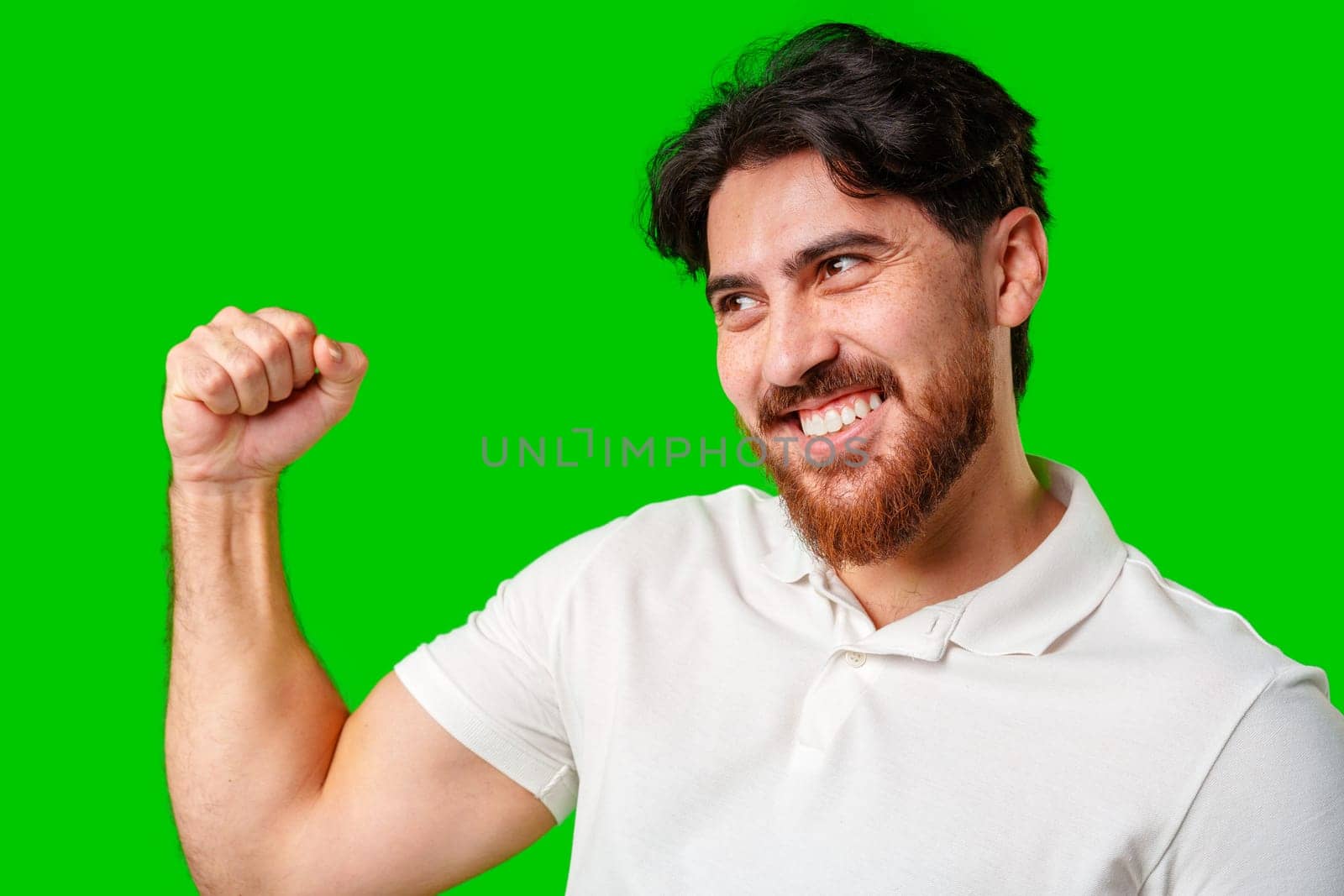 Happy man celebrating success with raised fists, wearing a white shirt against a bright green background close up