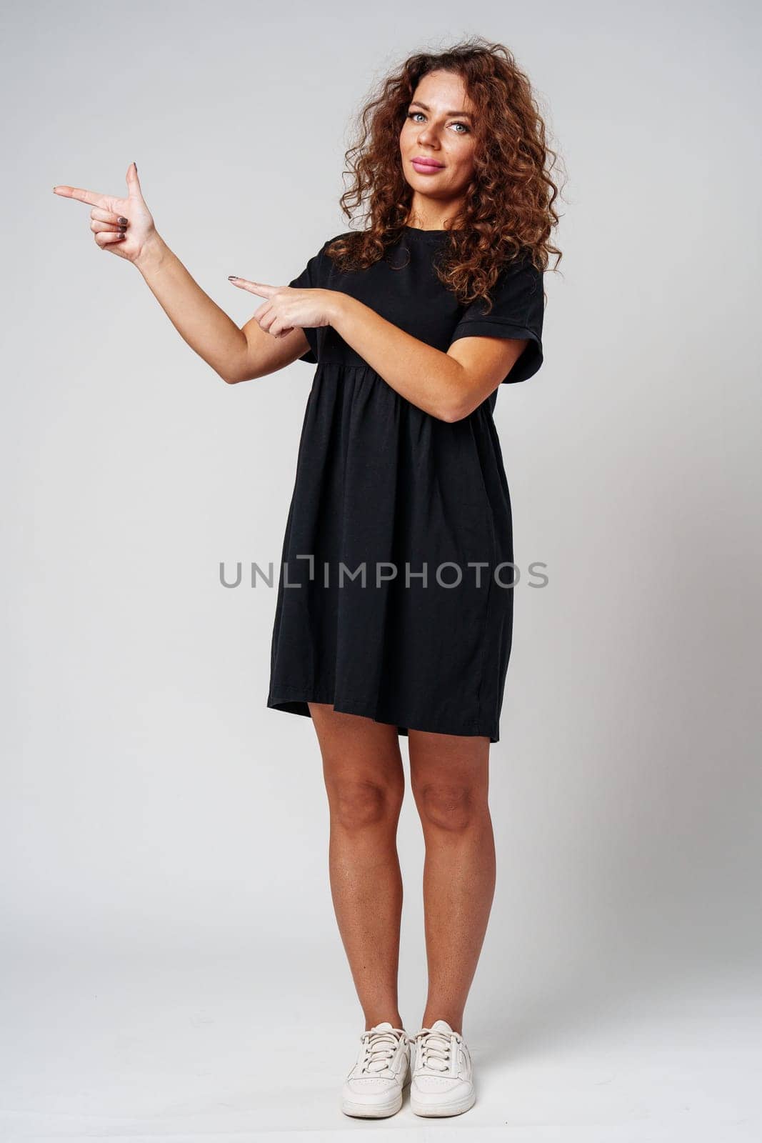 Cheerful woman with curly hair gestures playfully against a light gray background close up