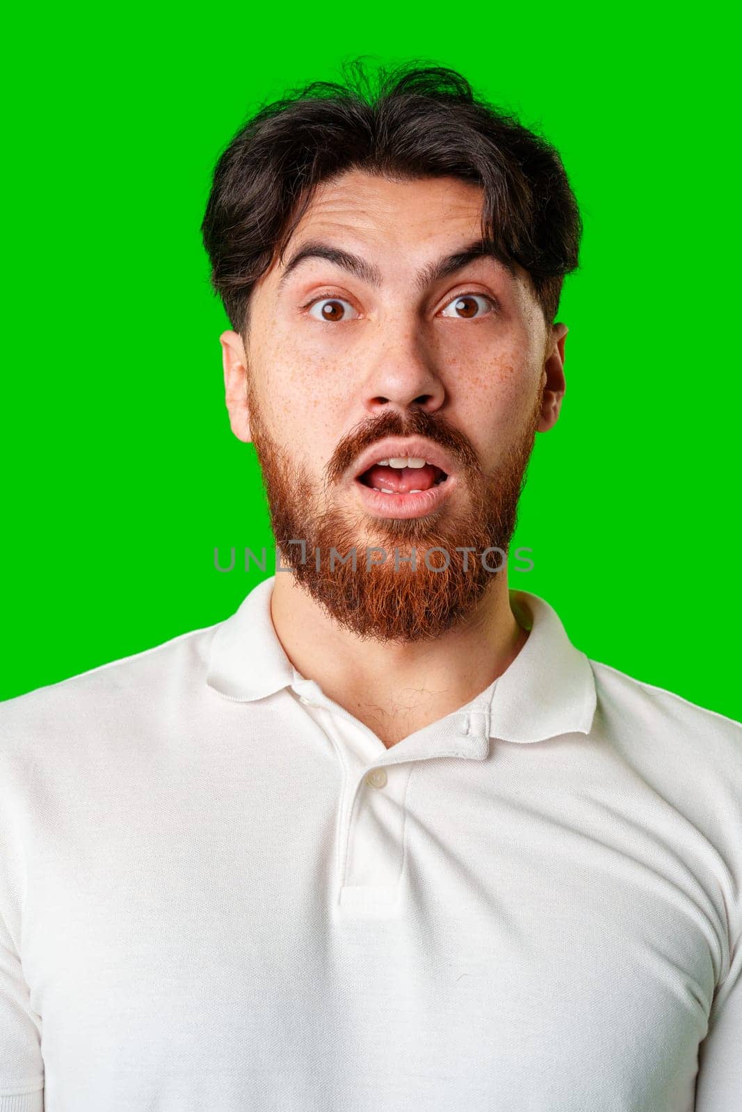 Surprised young man with a beard expressing shock against a bright green background in a casual setting