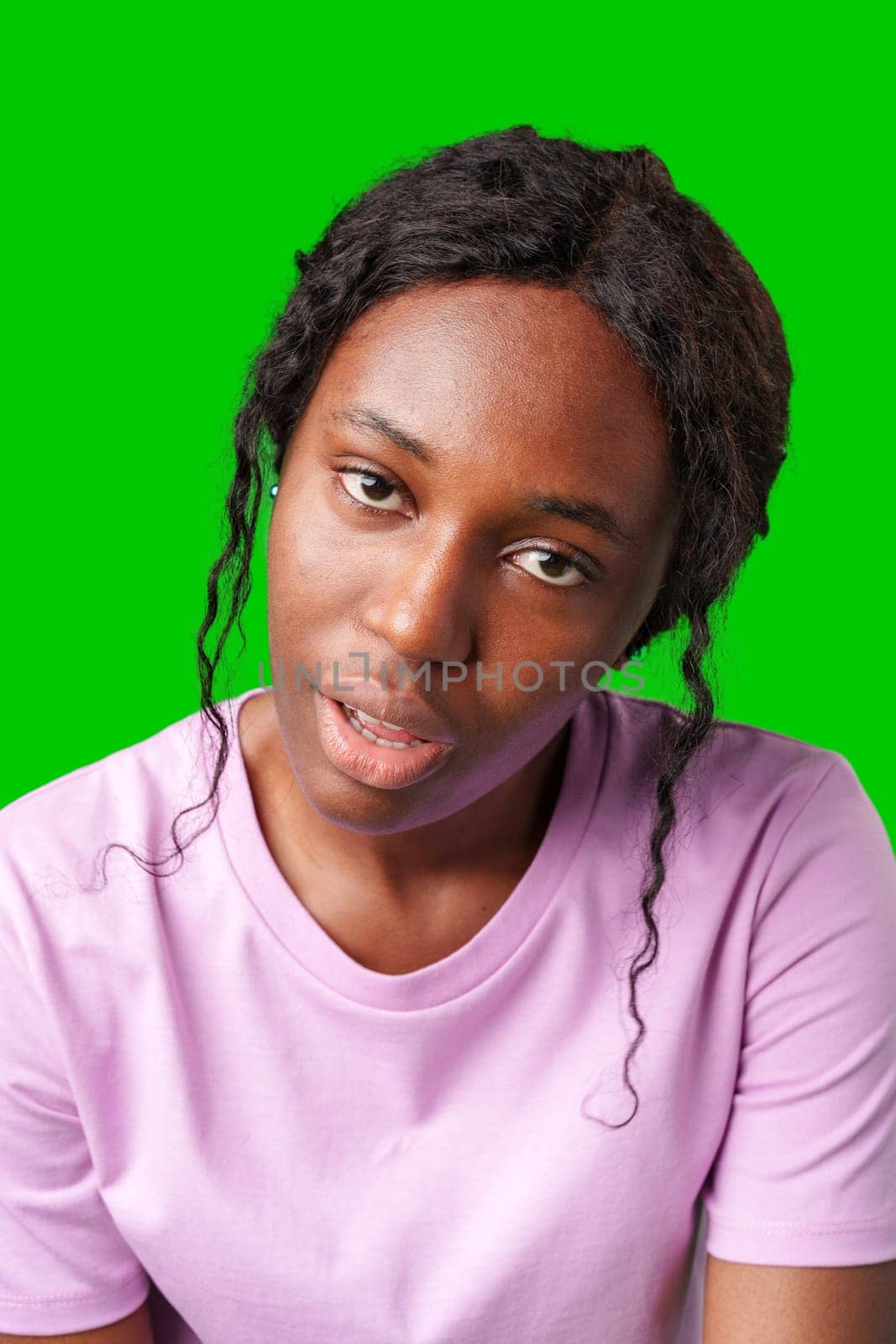Young woman with curly hair shows a skeptical expression against a bright green background in studio