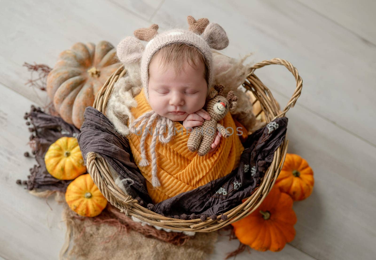 Newborn baby girl swaddled in white fabric sleeping in basket decorated with pumpkins. Infant child kid napping on fur autumn studio portrait