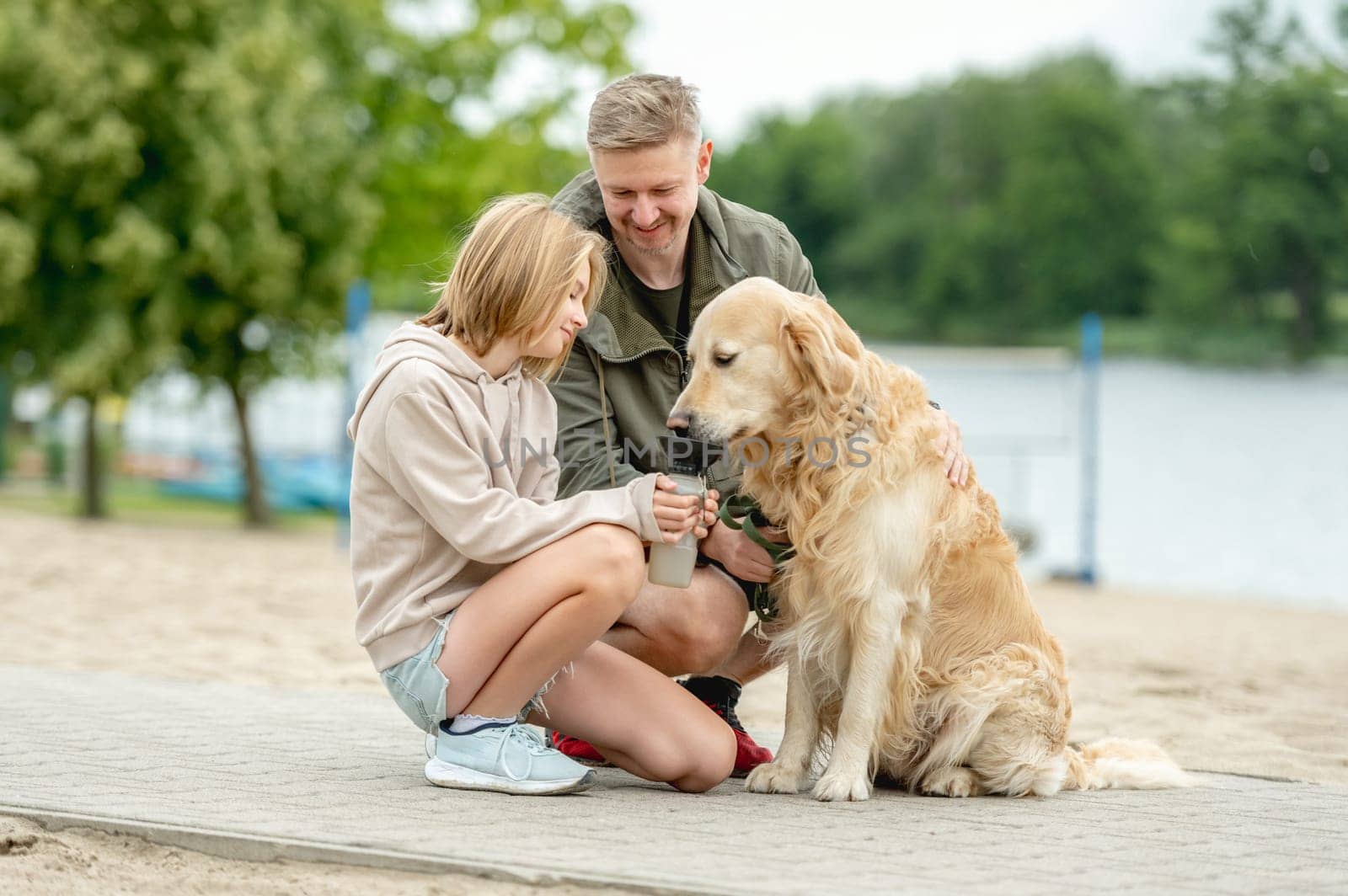 Girl With Dad Gives Golden Retriever A Drink While On A Walk