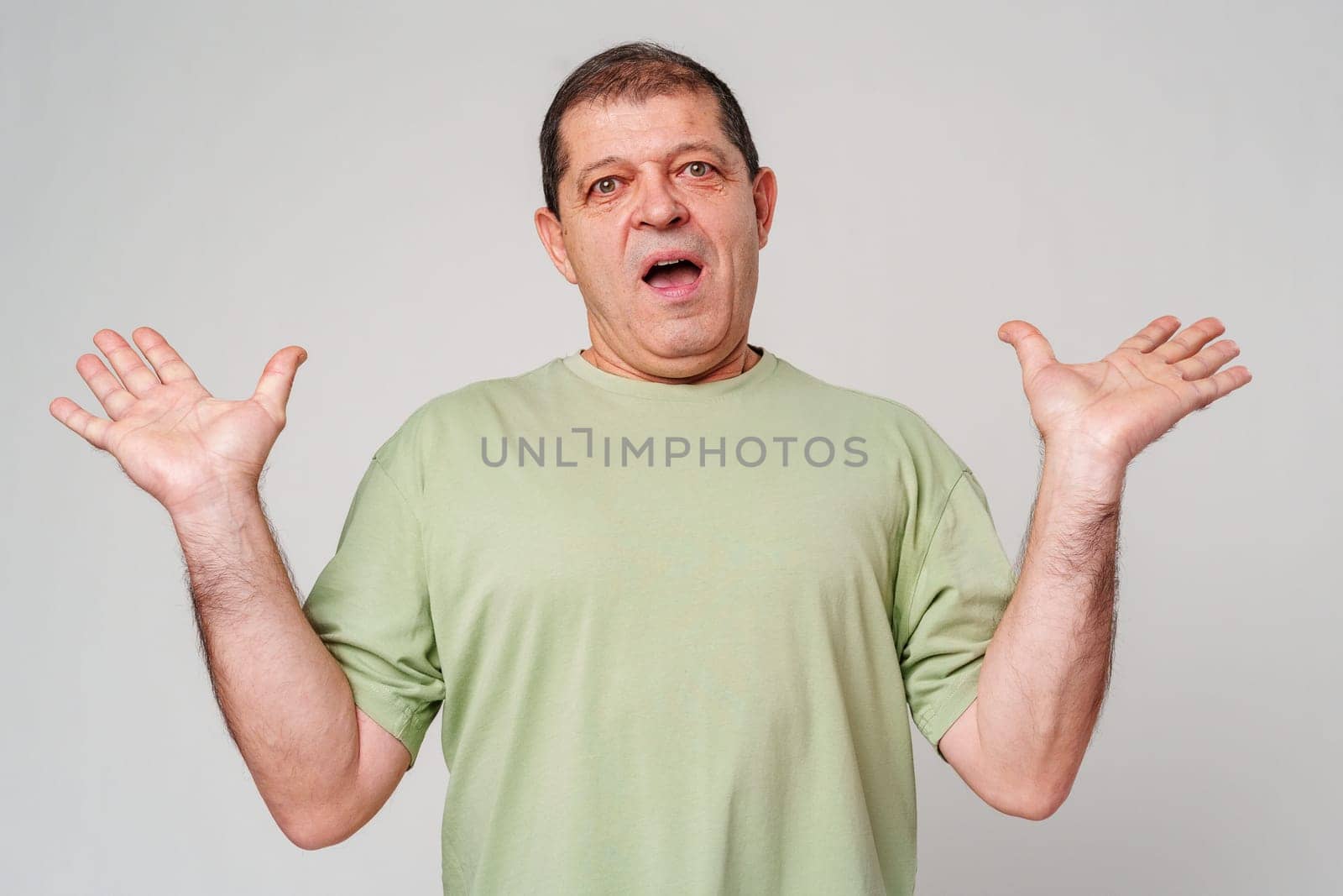 A surprised man in a green shirt expressing astonishment against a light background close up
