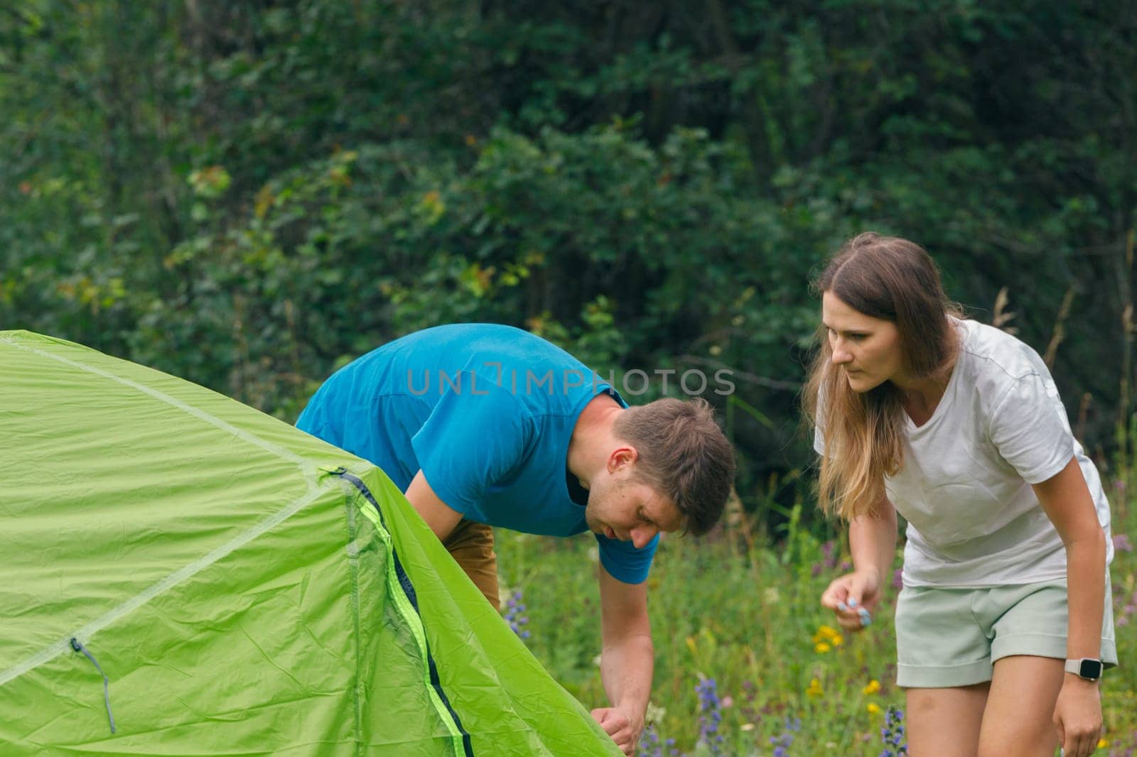 A couple enjoys a delightful camping experience by setting up their vibrant green tent amidst a picturesque landscape