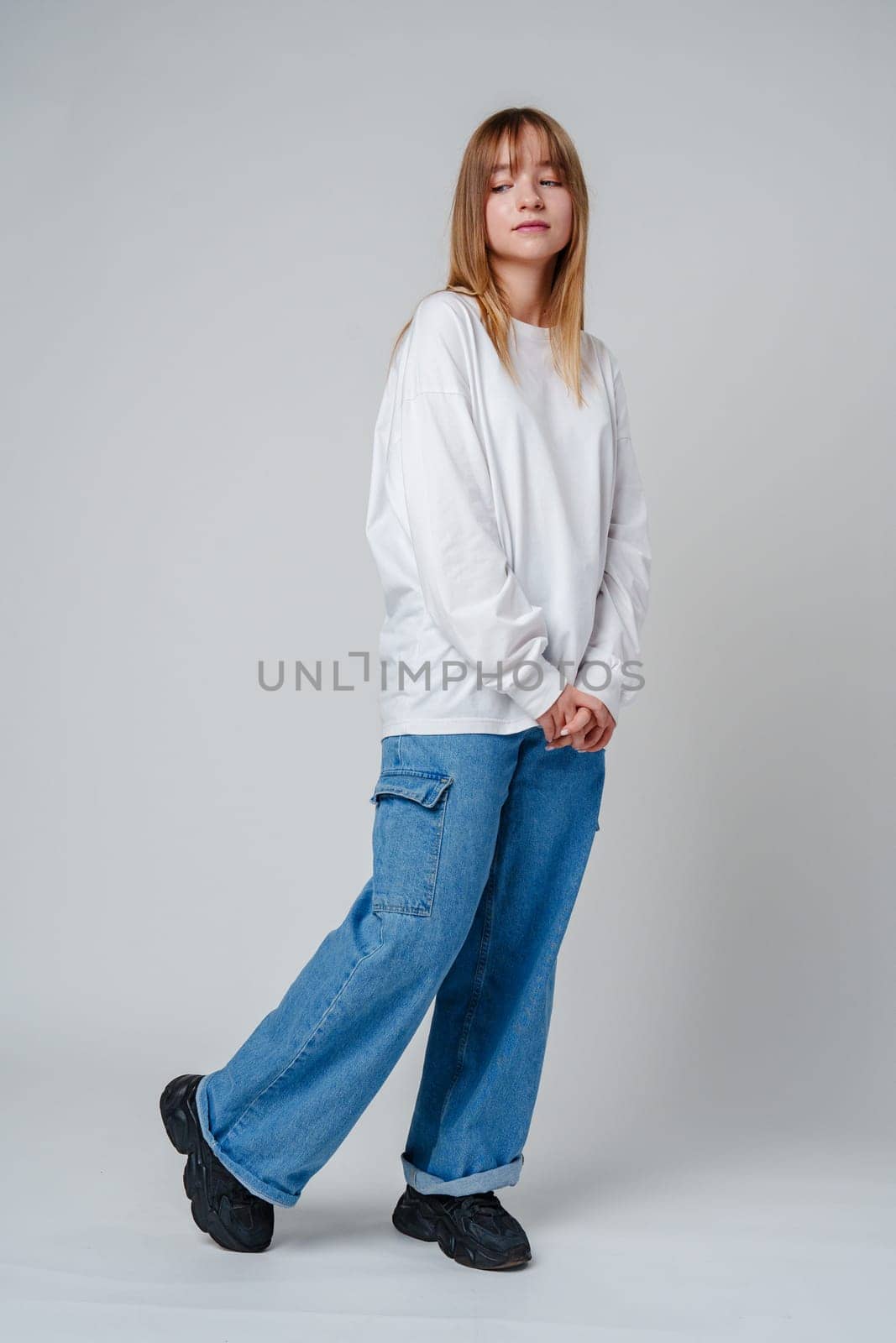 Teen girl stands in casual attire against a plain background, showcasing her thoughtful expression close up