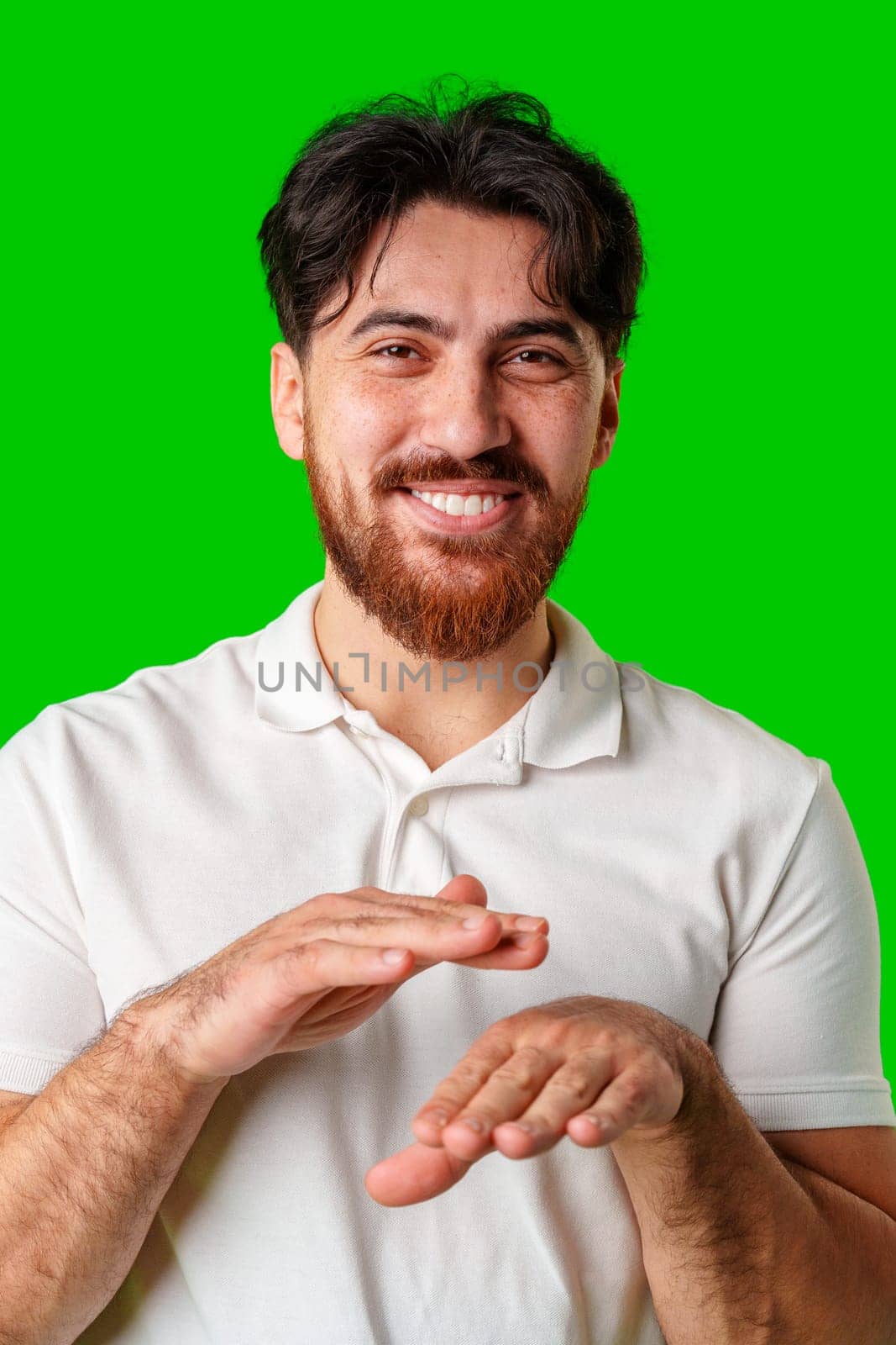 A young man in a white polo shirt dances energetically against a vibrant green background close up
