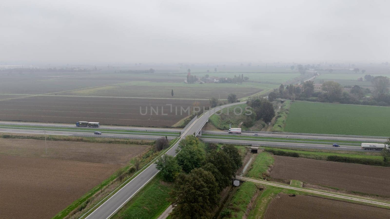 Piacenza, Italy October 15th 2024 Aerial view of a highway with cars and trucks passing over a countryside road on a foggy day