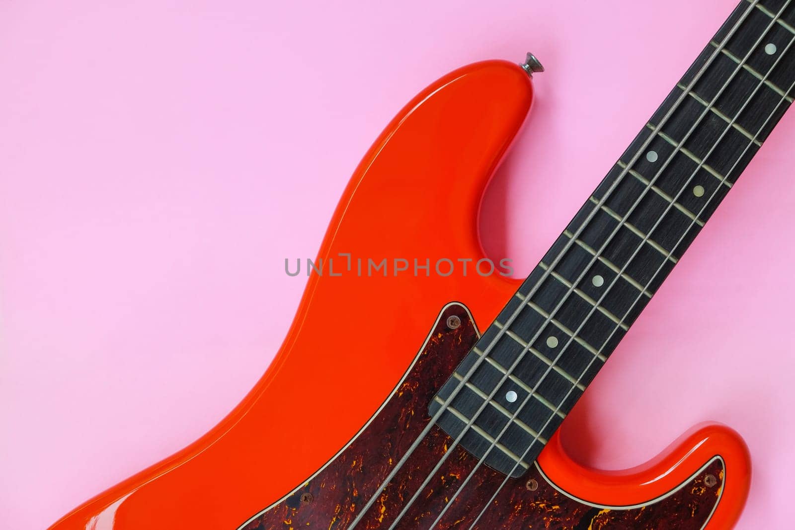 Red electric bass guitar on a pink background. Close-up image.