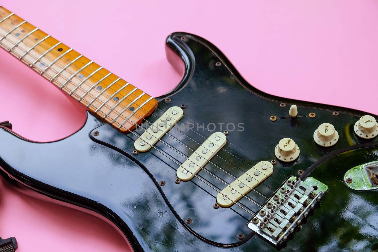 Black electric guitar on pink background. Top view with copy space.