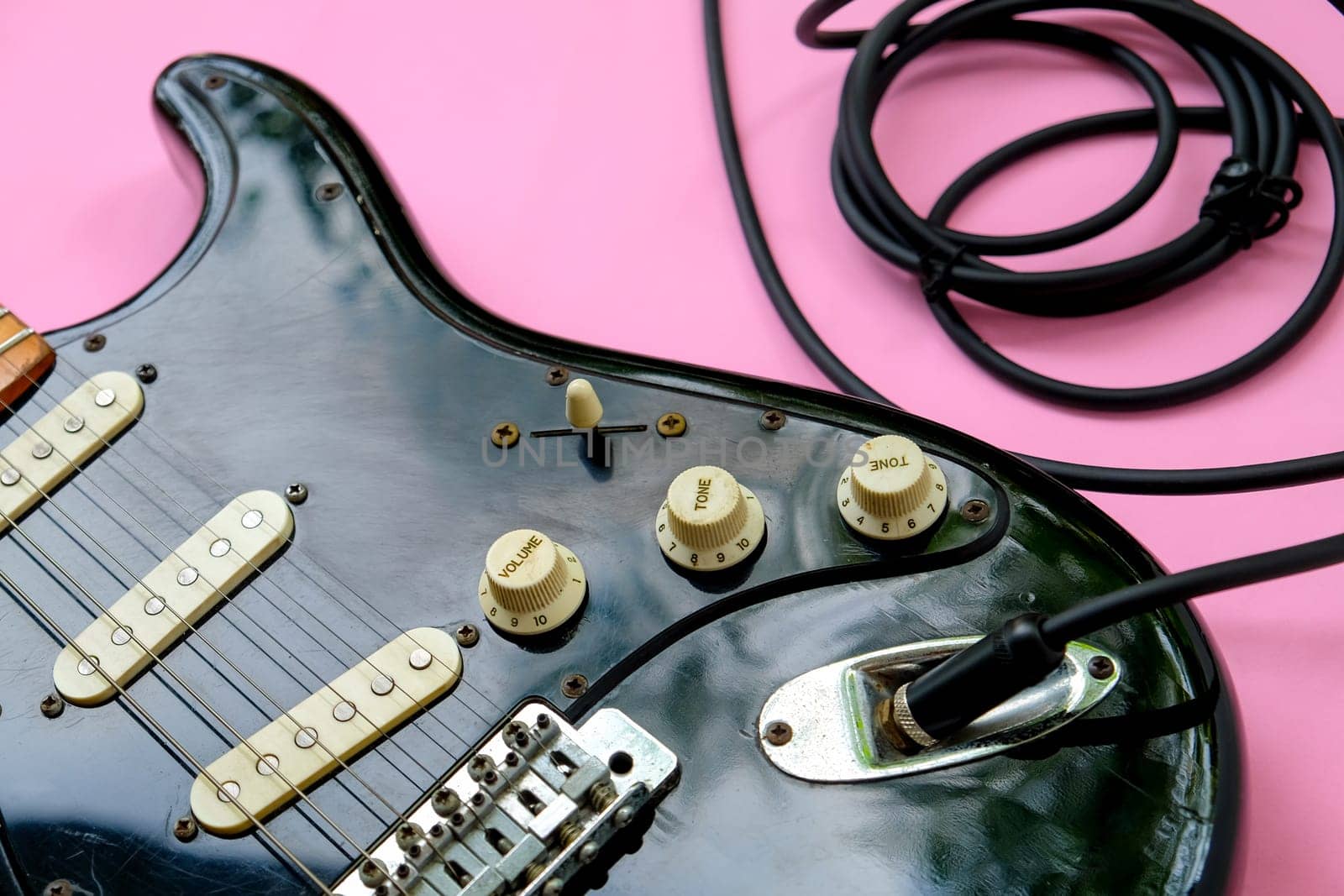 Electric guitar with cable on pink background, close-up image.