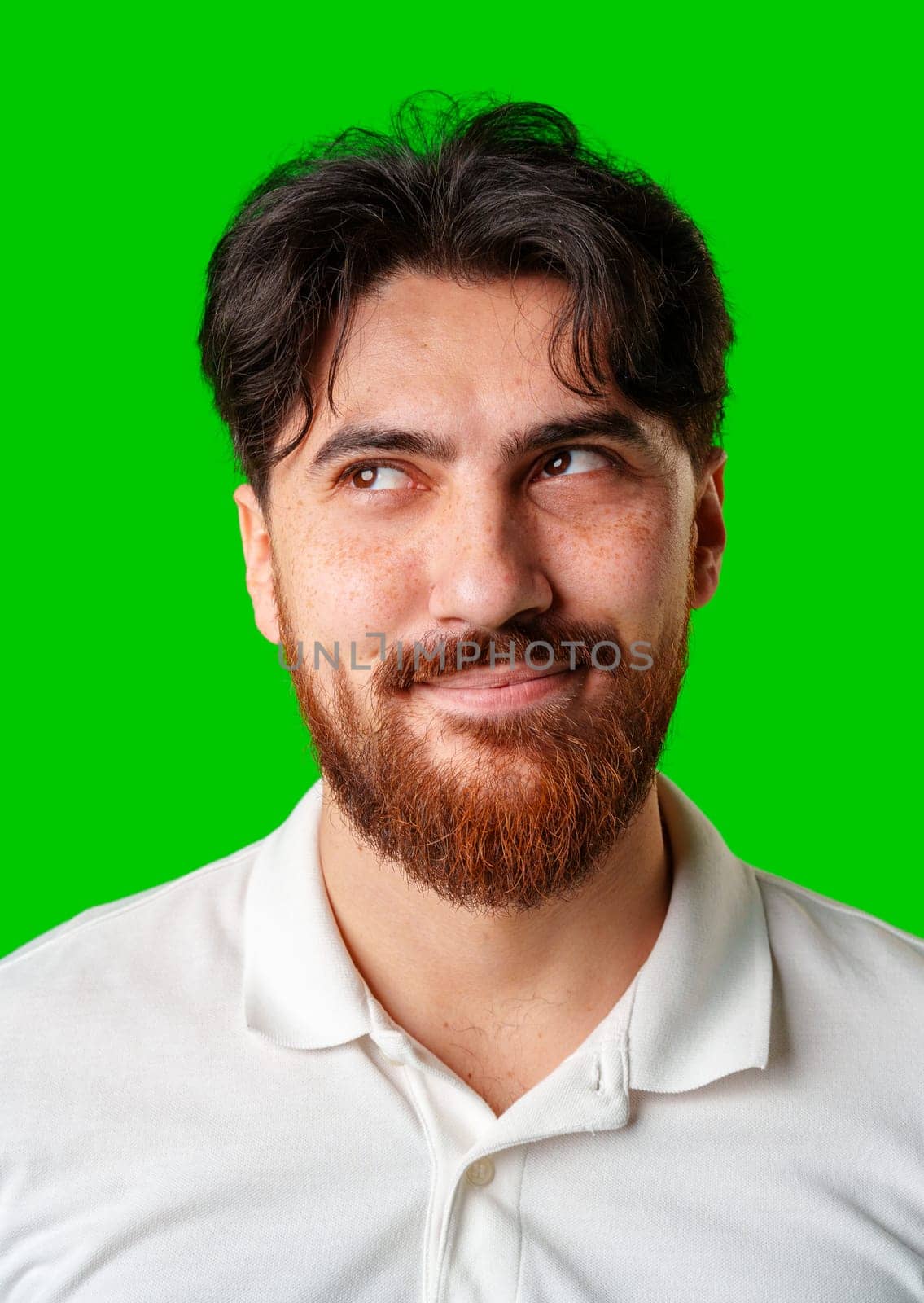 A smiling young man with a beard poses against a bright green background close up