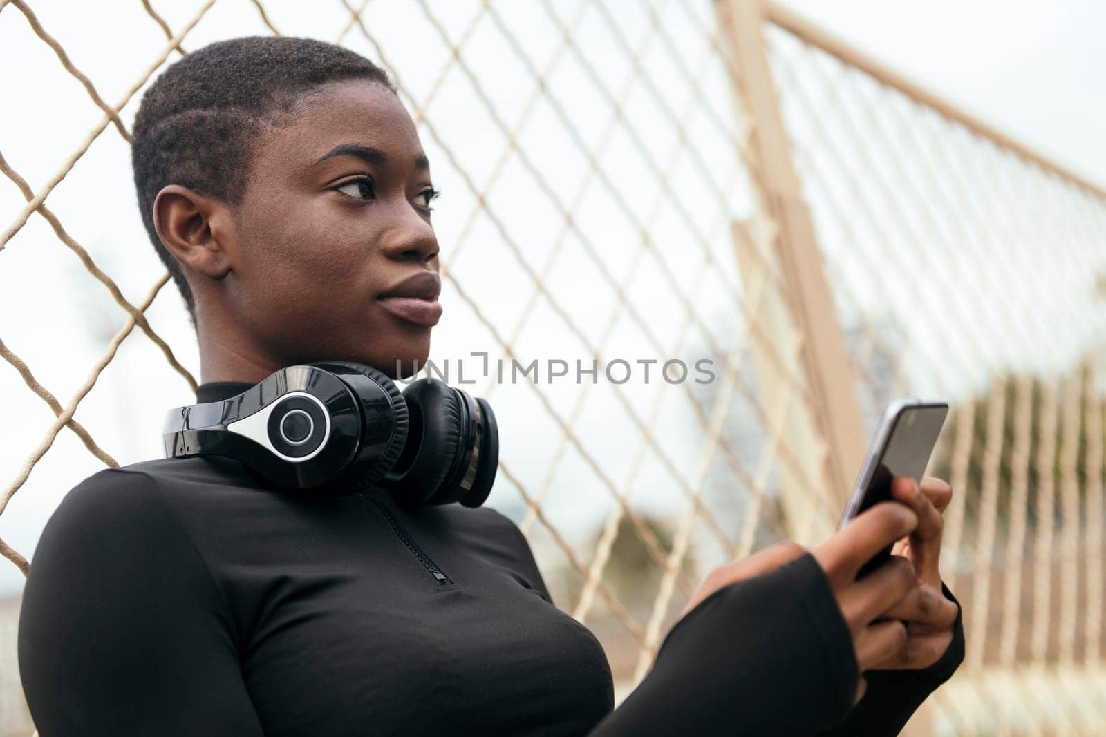 young glad ethnic female in wireless headphones surfing internet on cellphone, concept of technology of communication and urban lifestyle