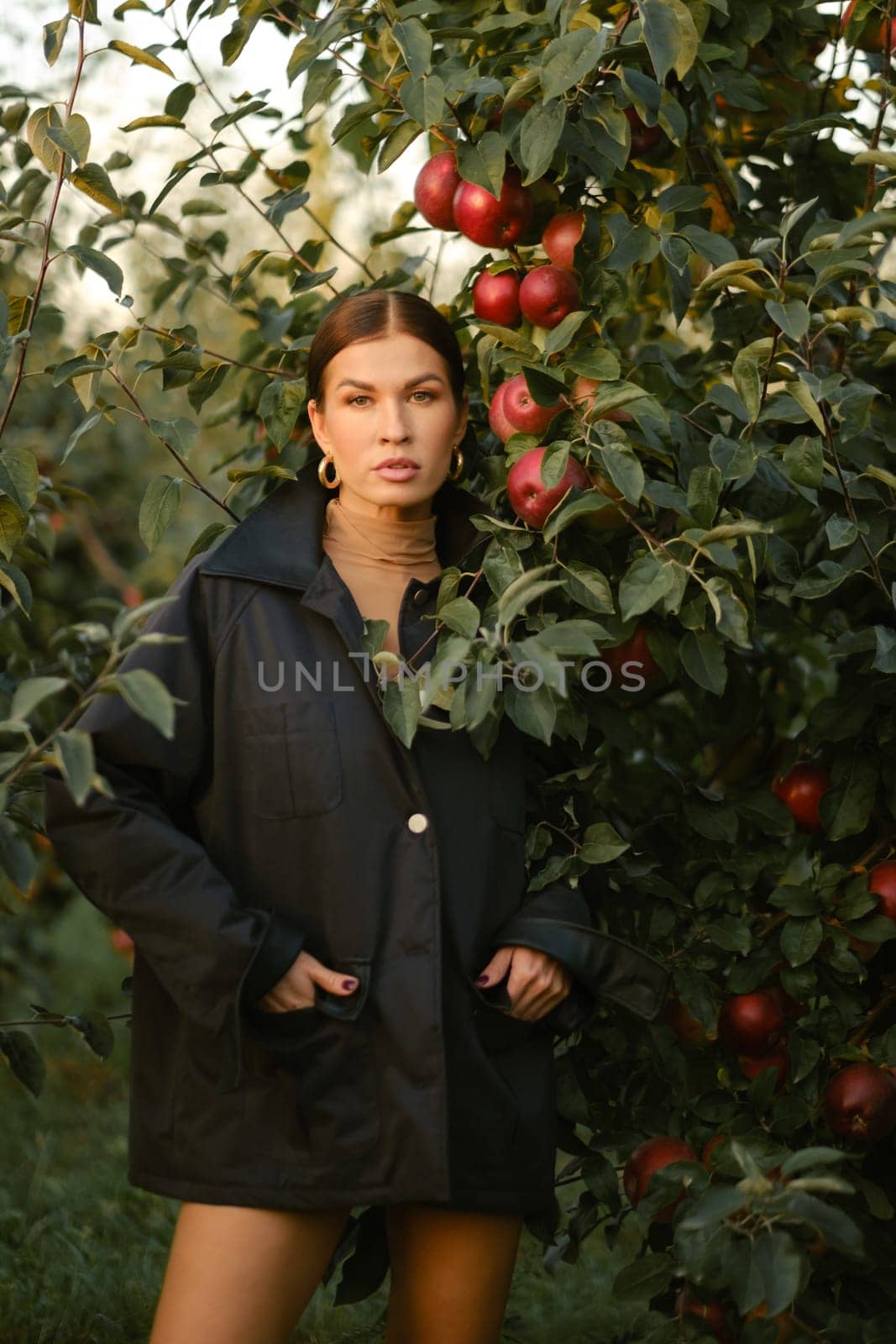 A beautiful girl in a black autumn jacket in an apple orchard. A fashionable girl at a fashion show in the apple orchard.
