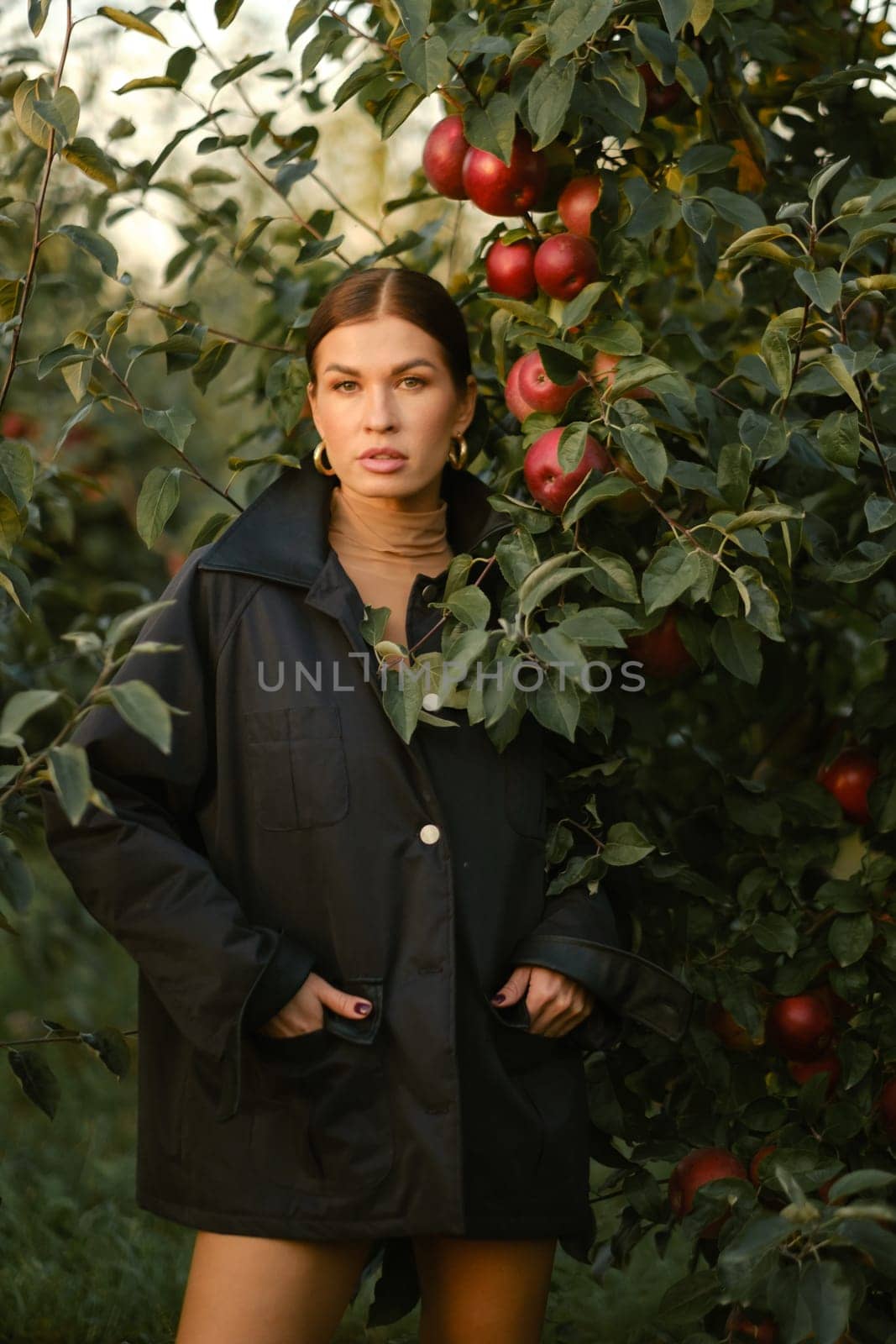 A beautiful girl in a black autumn jacket in an apple orchard. A fashionable girl at a fashion show in the apple orchard.