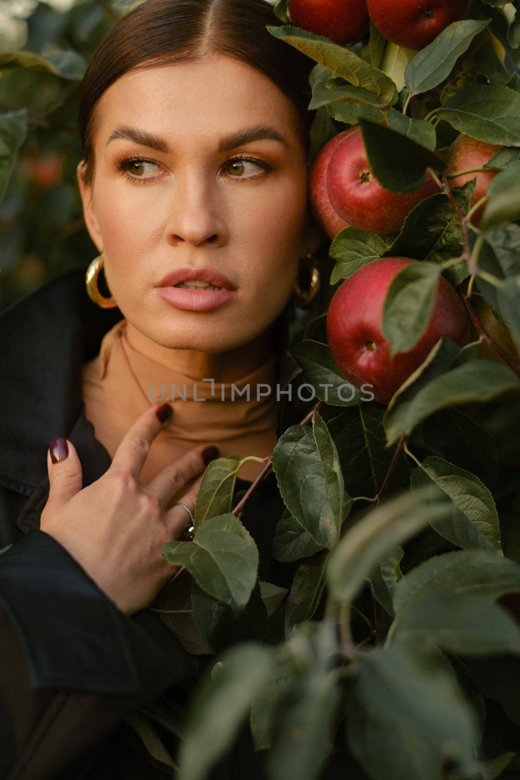 A beautiful girl in a black autumn jacket in an apple orchard. A fashionable girl at a fashion show in the apple orchard.