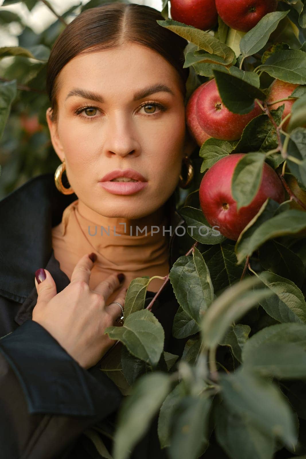 Close-up of a girl's face in an apple orchard. A fashionable girl on the background of a tree with red apples.