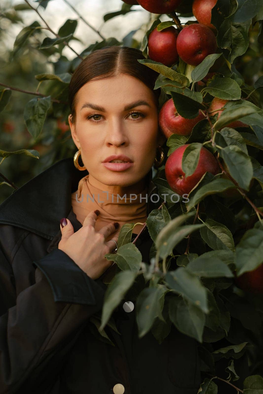 A beautiful girl in a black autumn jacket in an apple orchard. A fashionable girl at a fashion show in the apple orchard.